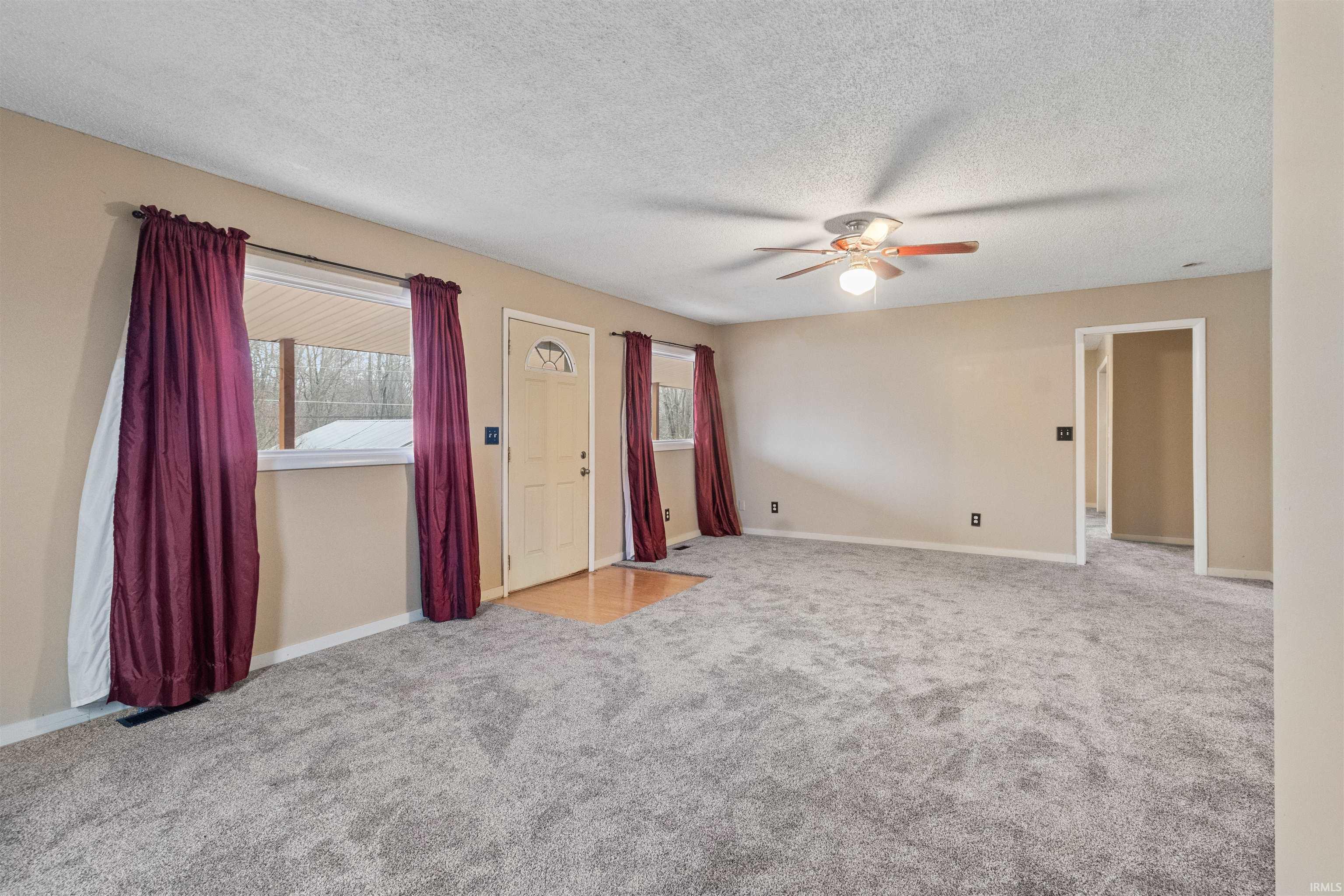 Unfurnished living room featuring carpet floors, a textured ceiling, and a ceiling fan