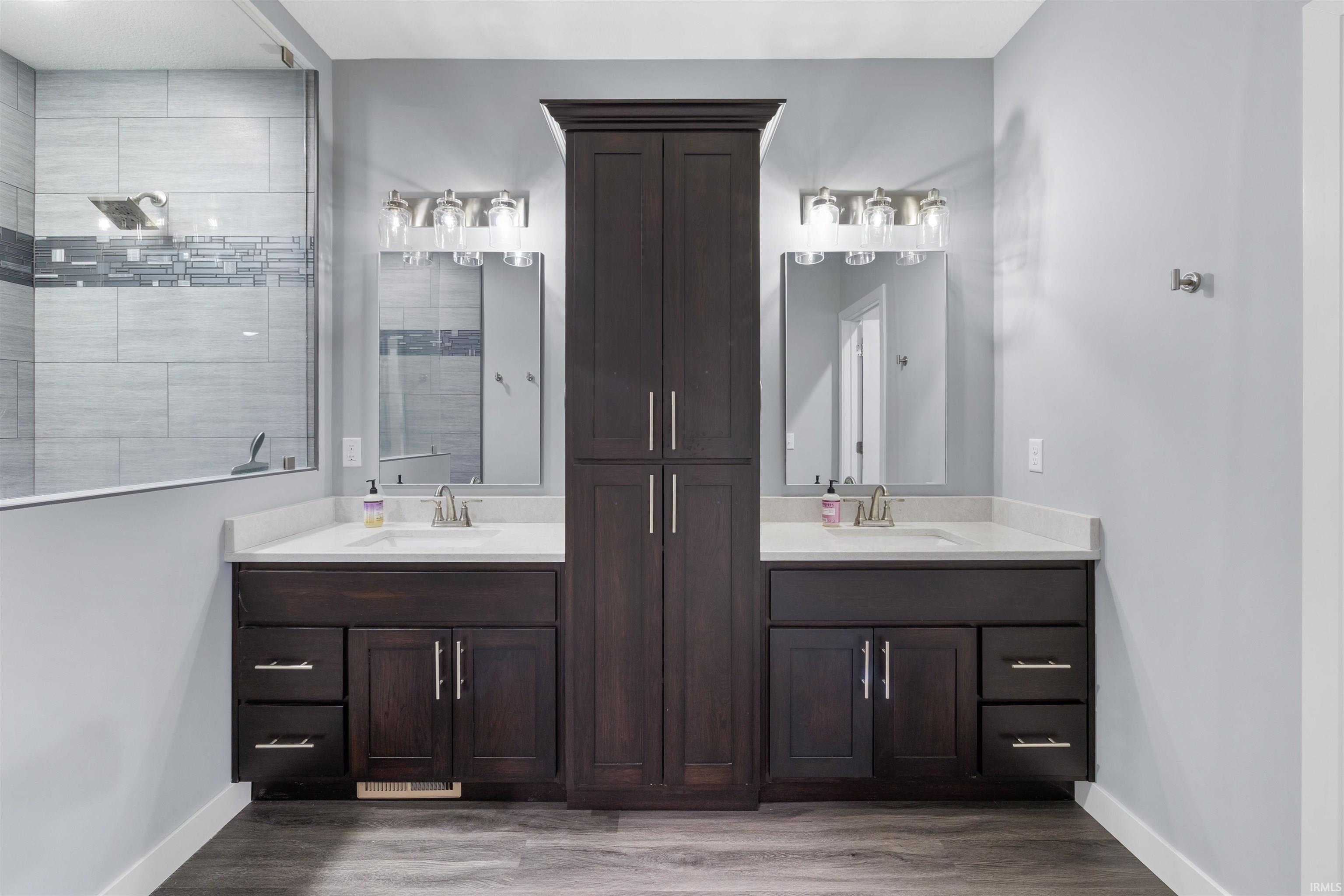 Full bath with two vanities, dark wood-style flooring, and a walk in shower