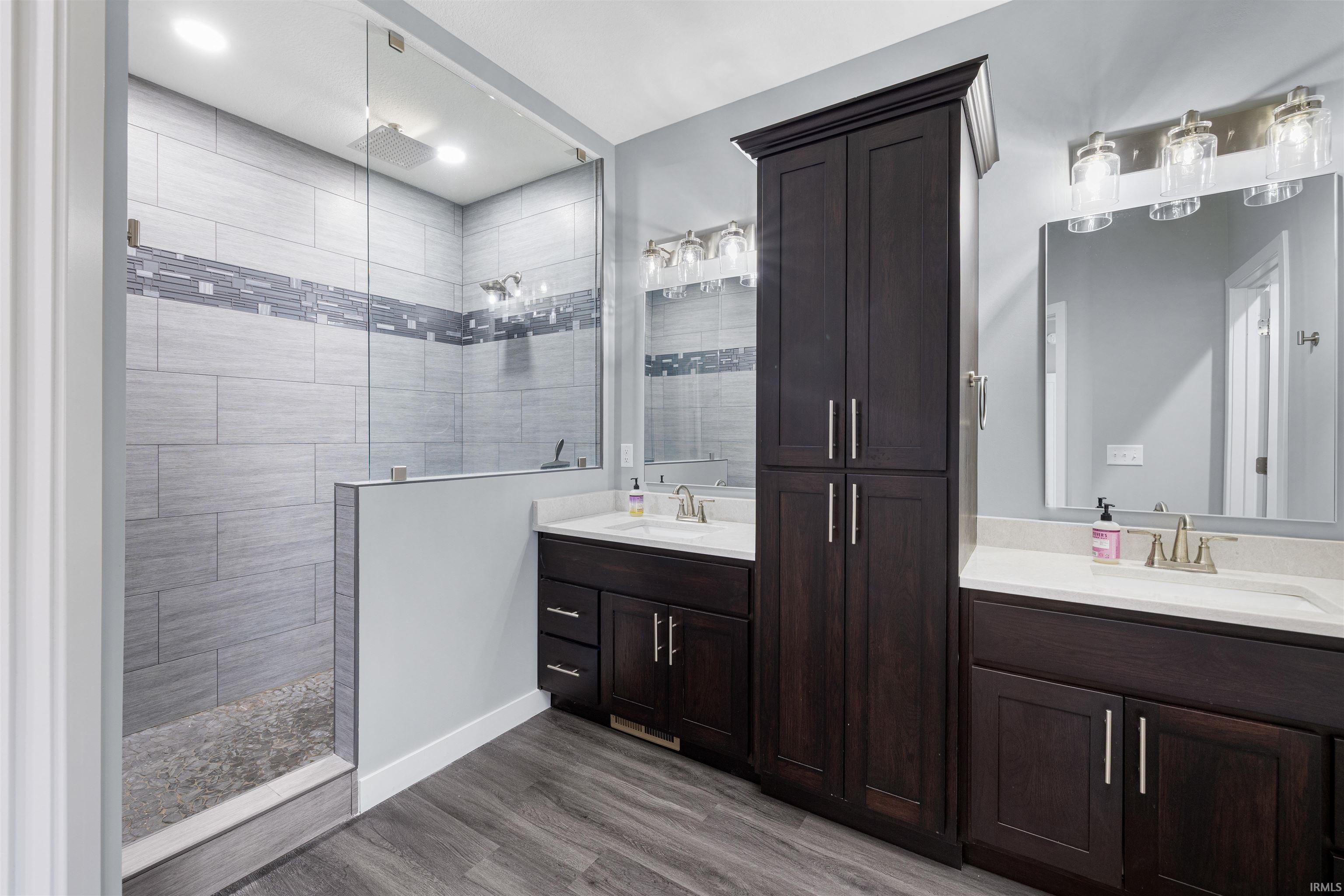 Bathroom featuring two vanities, walk in shower, and dark wood finished floors