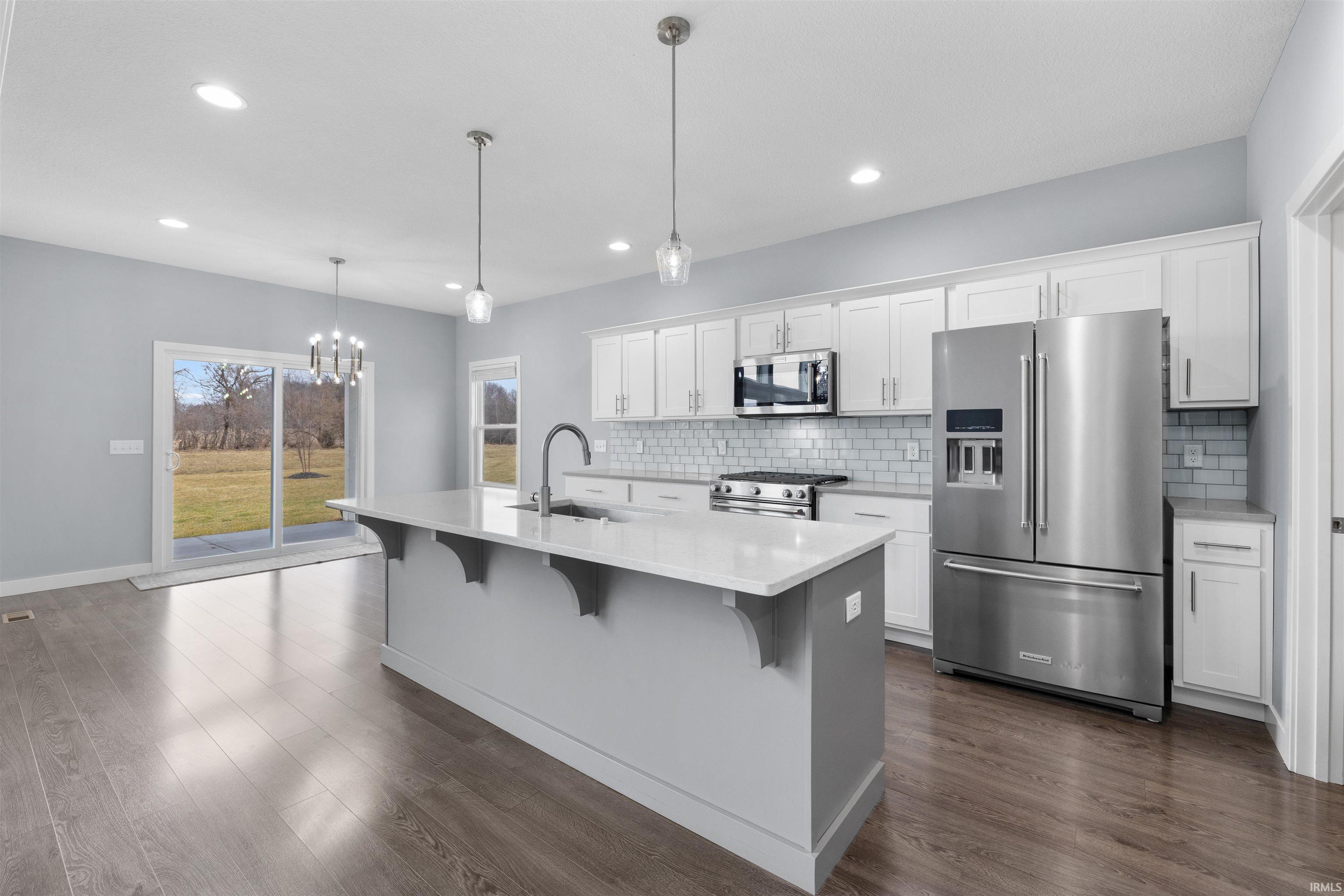 Kitchen featuring premium appliances, suspended lighting, a kitchen breakfast bar, dark wood-style flooring, and a center island with sink