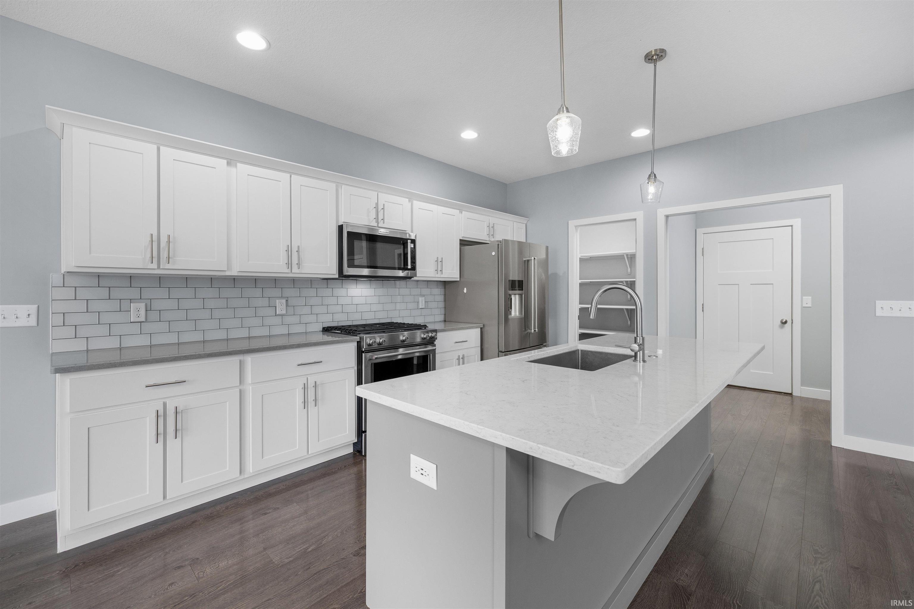 Kitchen with white cabinetry, an island with sink, stainless steel appliances, a kitchen breakfast bar, and light stone counters
