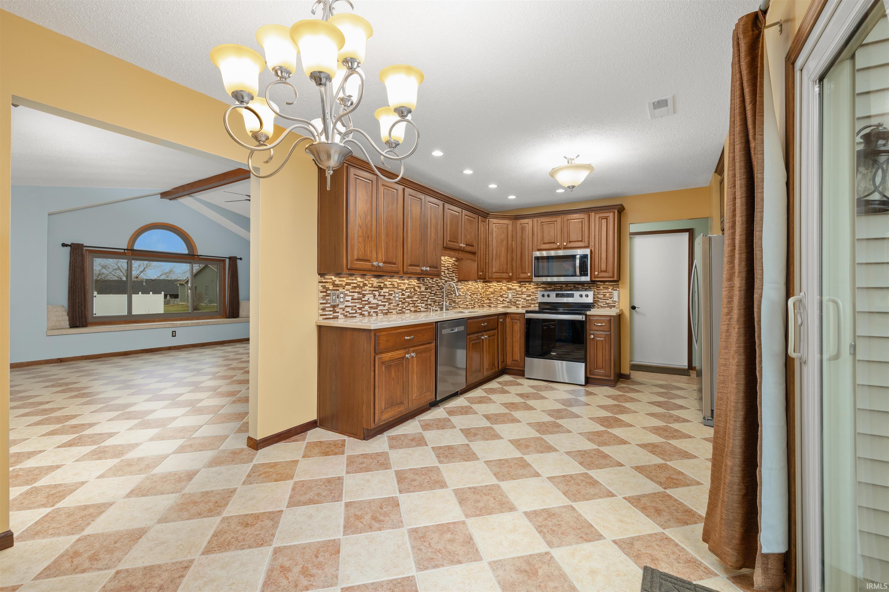Kitchen with wood finish cabinetry, stainless steel appliances, a chandelier, backsplash, and open floor plan
