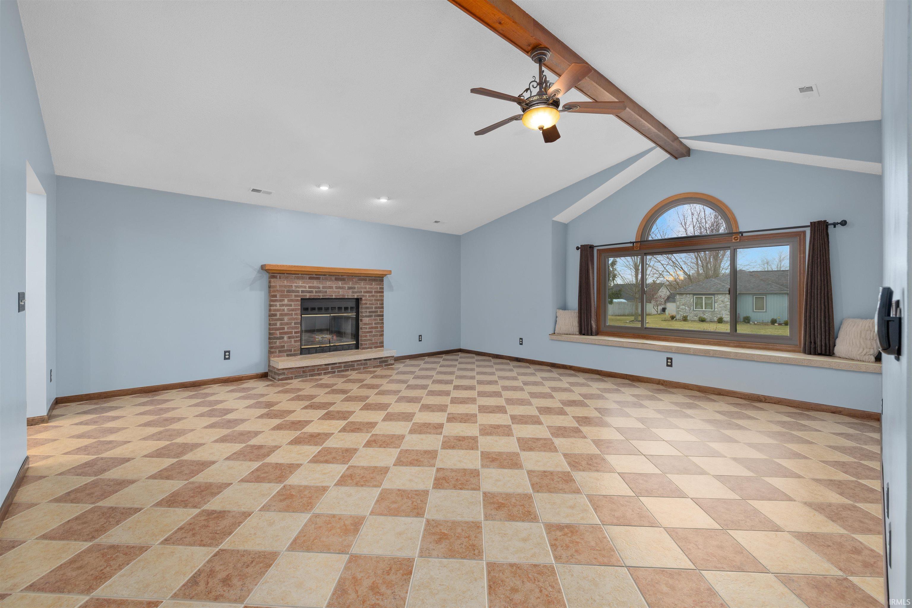 Unfurnished living room featuring beamed ceiling, a fireplace, and a ceiling fan