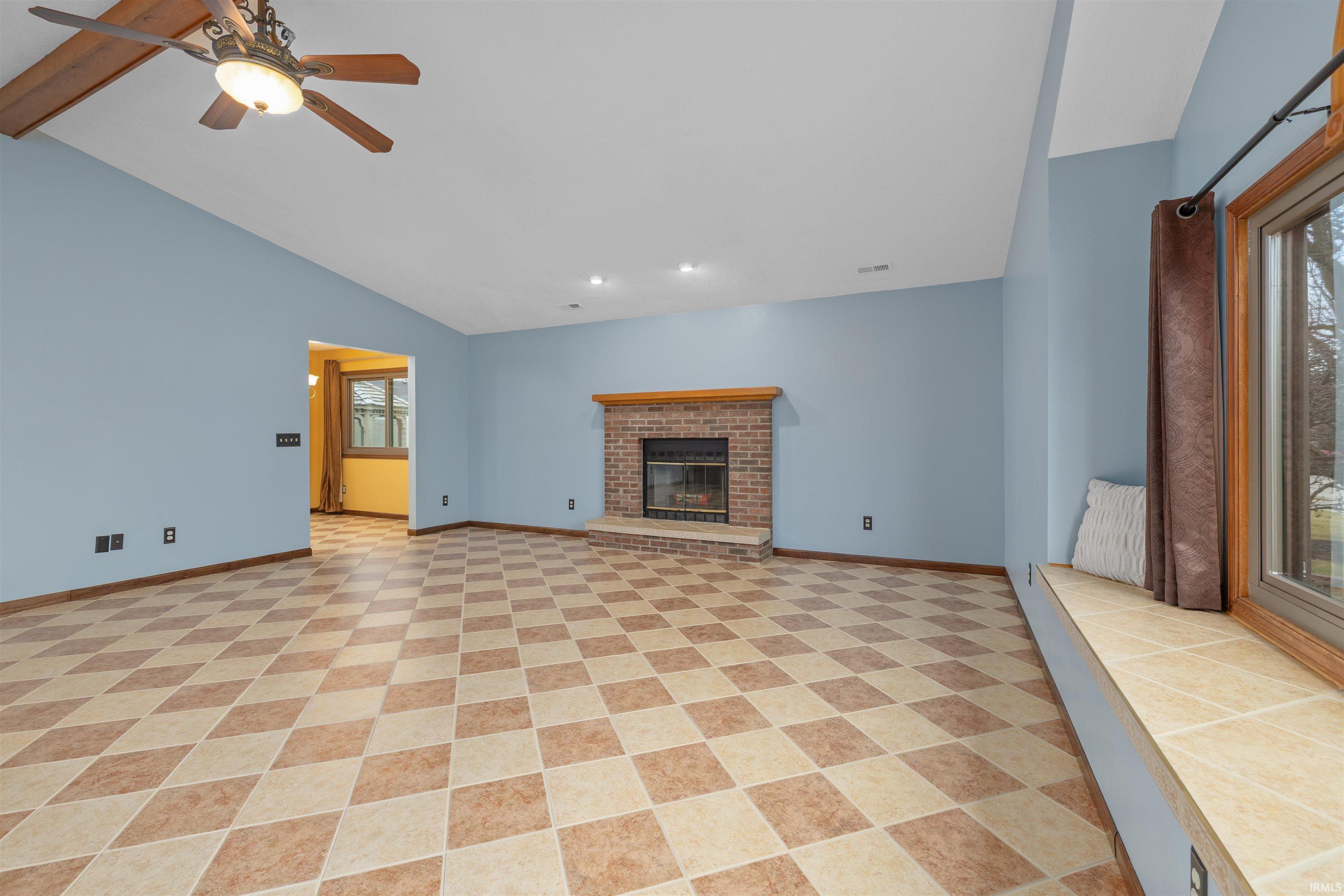 Unfurnished living room featuring a ceiling fan, a fireplace, and lofted ceiling with beams