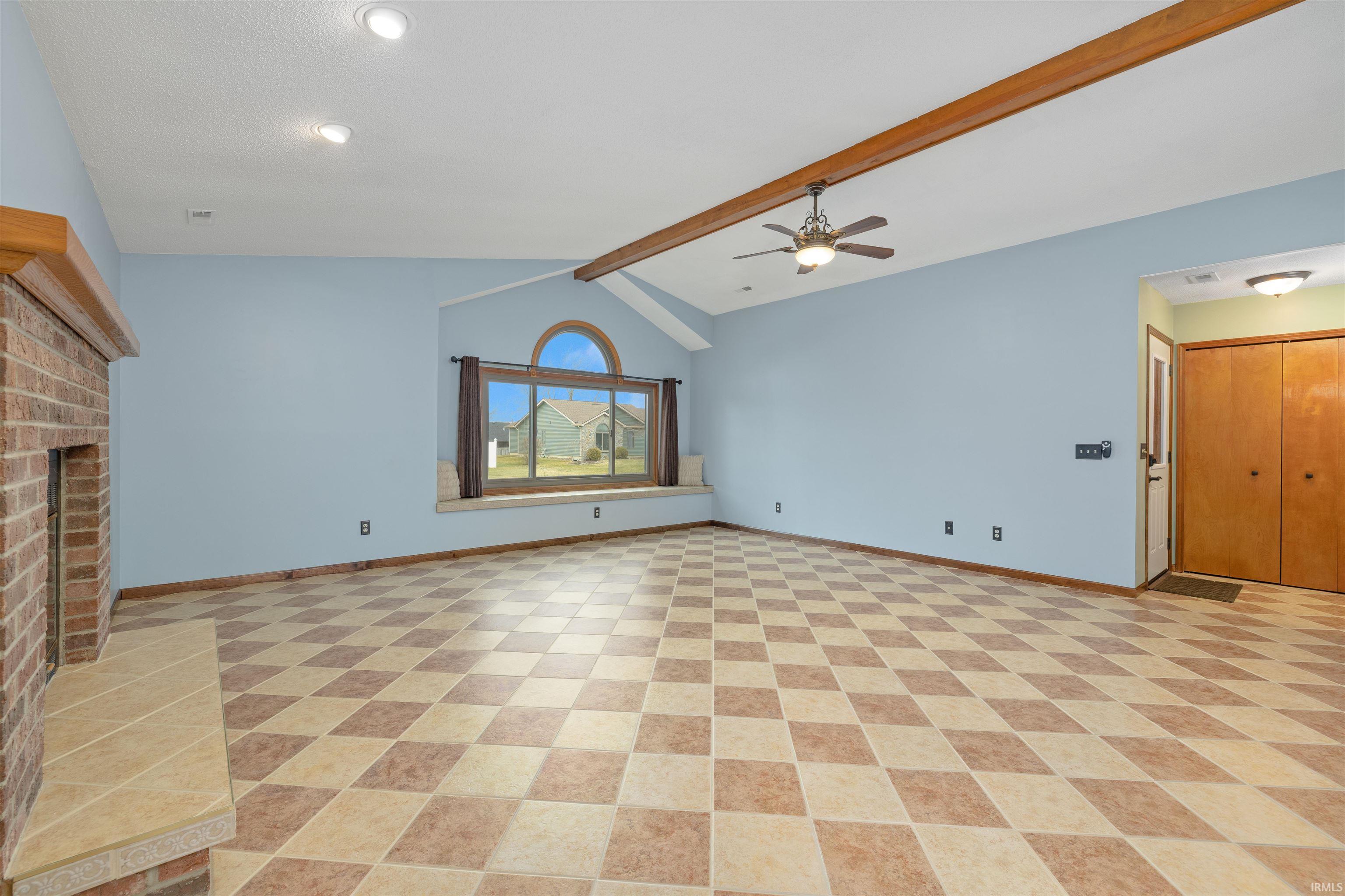 Unfurnished living room featuring beam ceiling, ceiling fan, and a brick fireplace