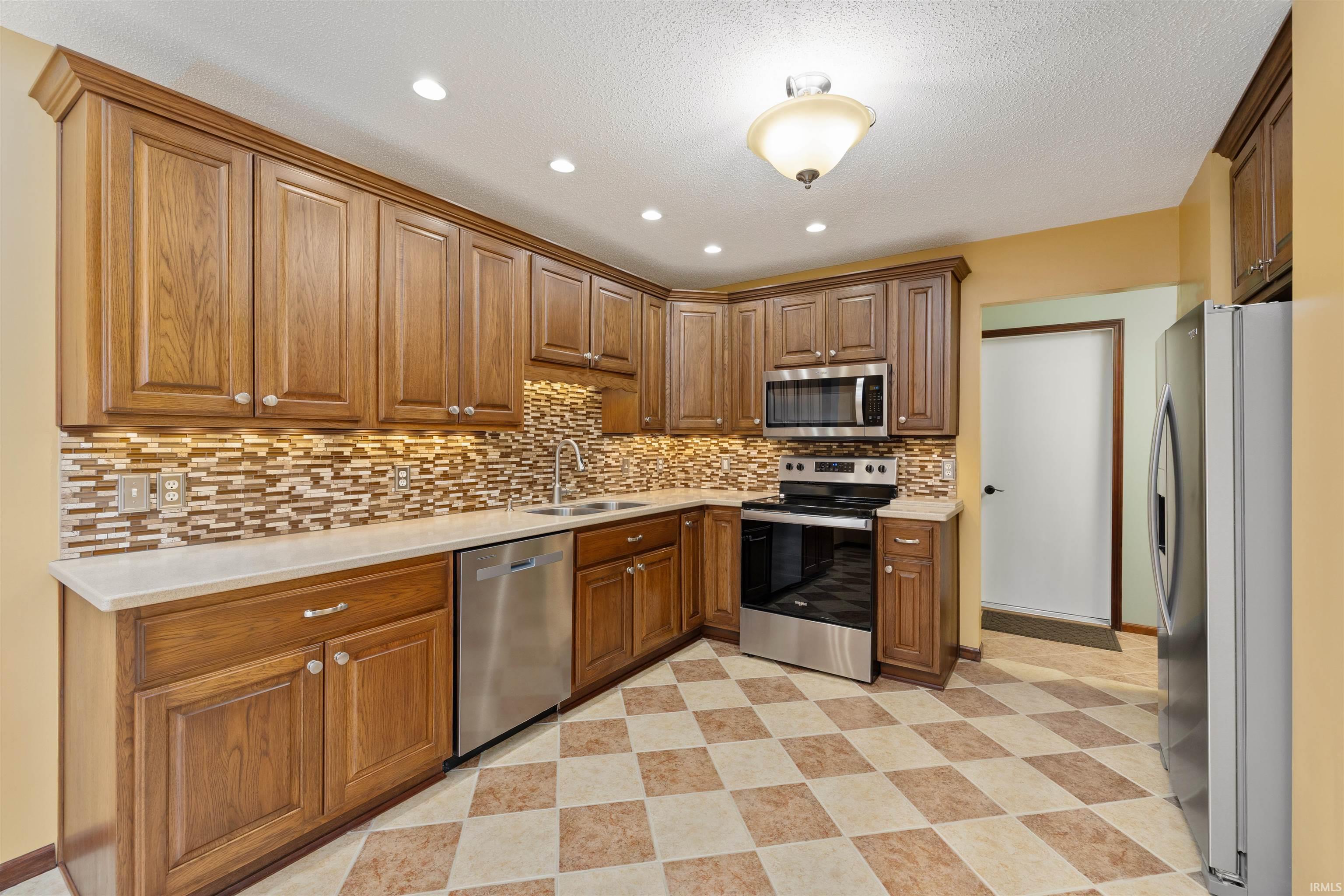 Kitchen featuring stainless steel appliances, wood finish cabinetry, recessed lighting, decorative backsplash, and light floors