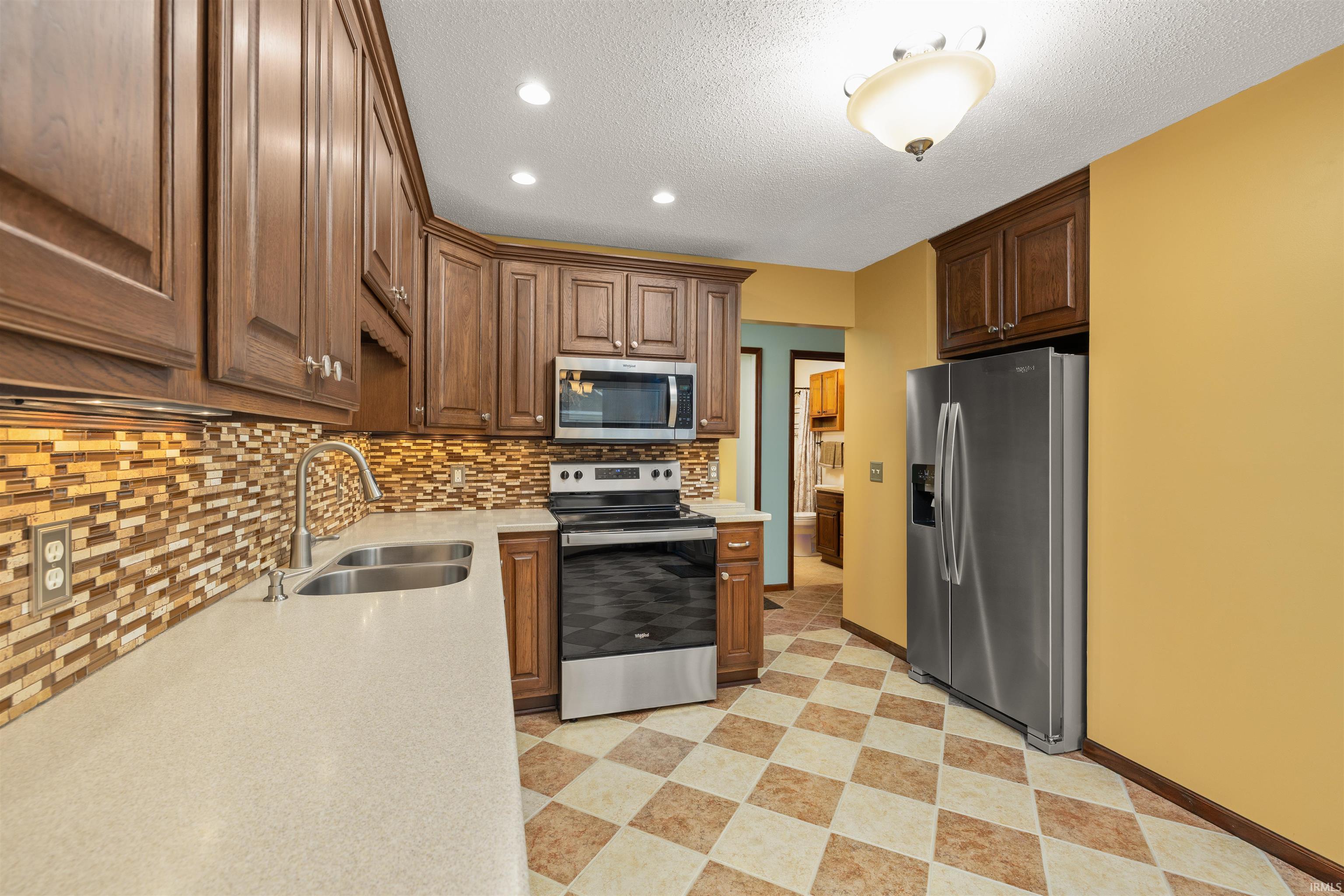 Kitchen with stainless steel appliances, light stone counters, a textured ceiling, light floors, and recessed lighting