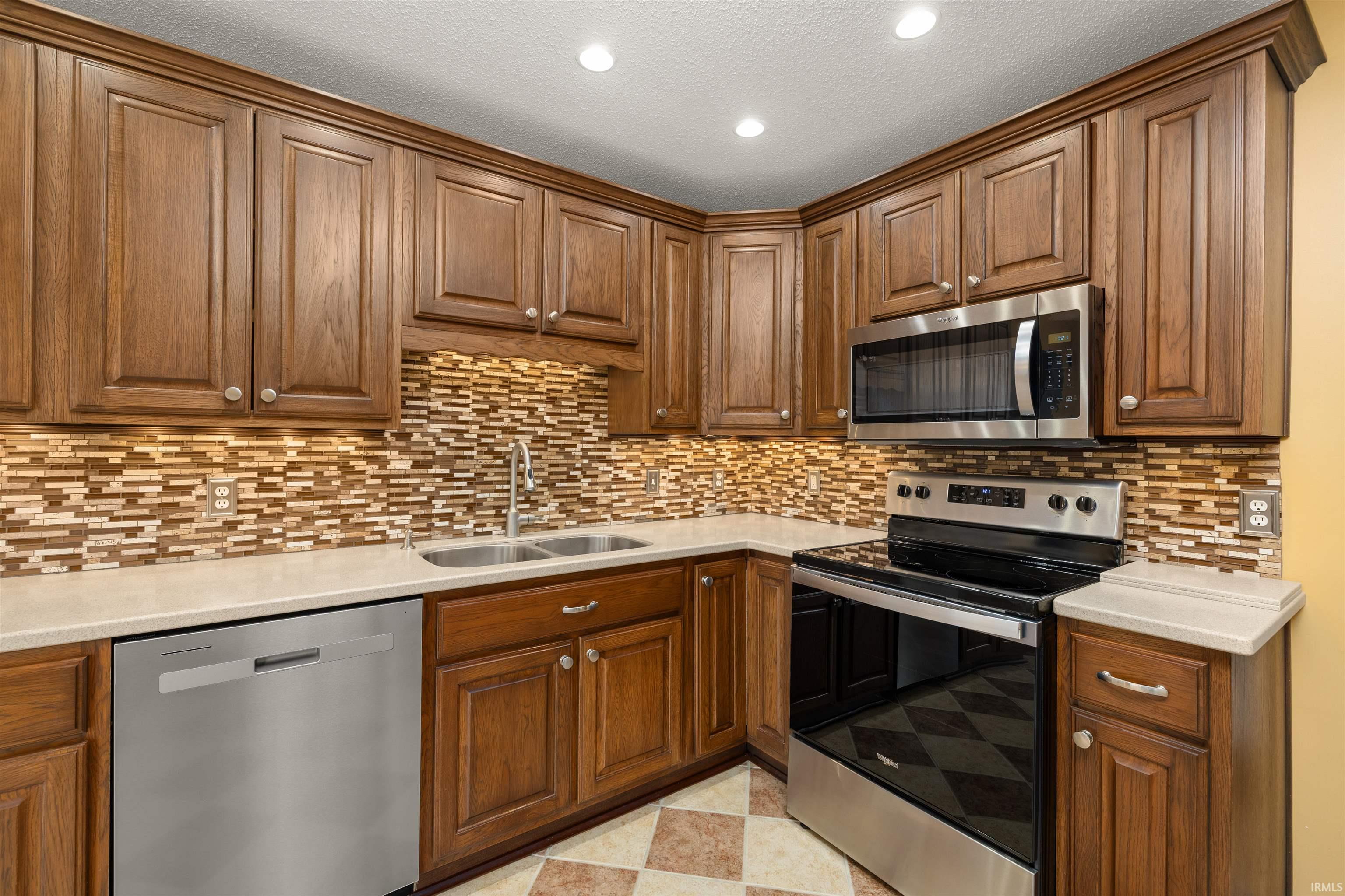 Kitchen featuring stainless steel appliances, wood finish cabinets, light flooring, light stone counters, and recessed lighting