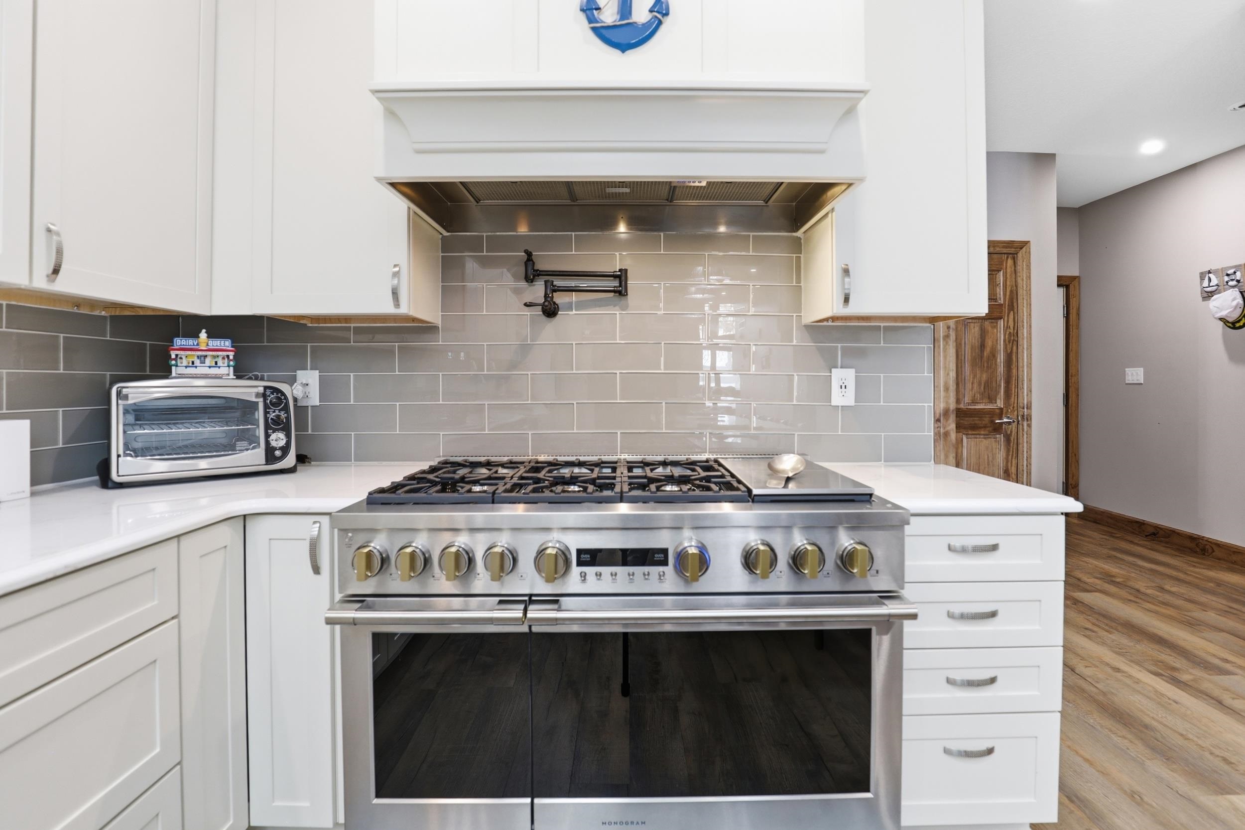 Kitchen with range with two ovens, white cabinetry, wood finished floors, light stone counters, and tasteful backsplash