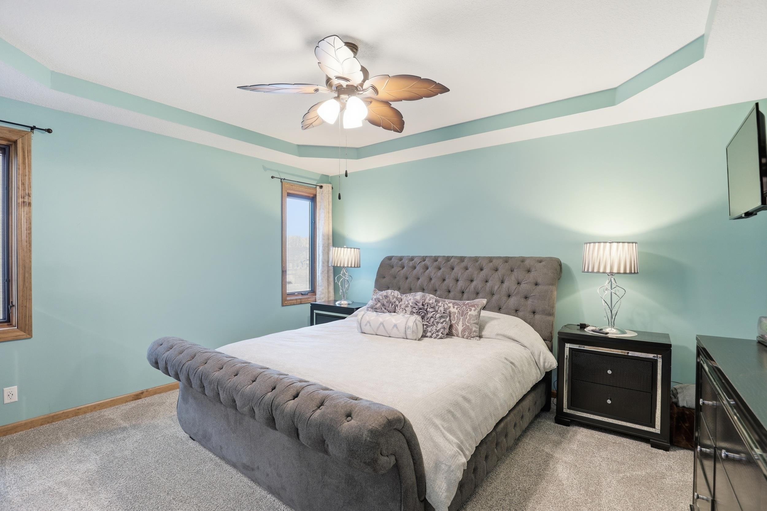 Bedroom with light colored carpet, ceiling fan, and a raised ceiling