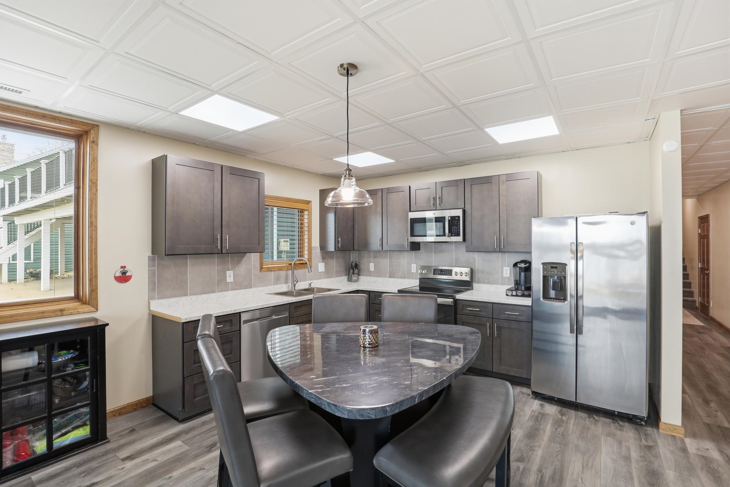 Kitchen featuring stainless steel appliances, dark wood finish cabinetry, pendant lighting, light wood-style flooring, and an ornate ceiling