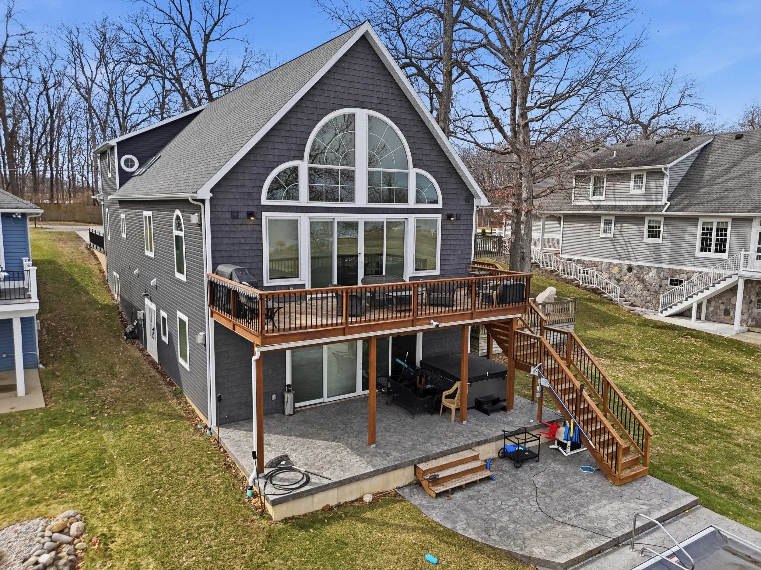 Back of house featuring a wooden deck, a lawn, a hot tub, a patio, and a shingled roof