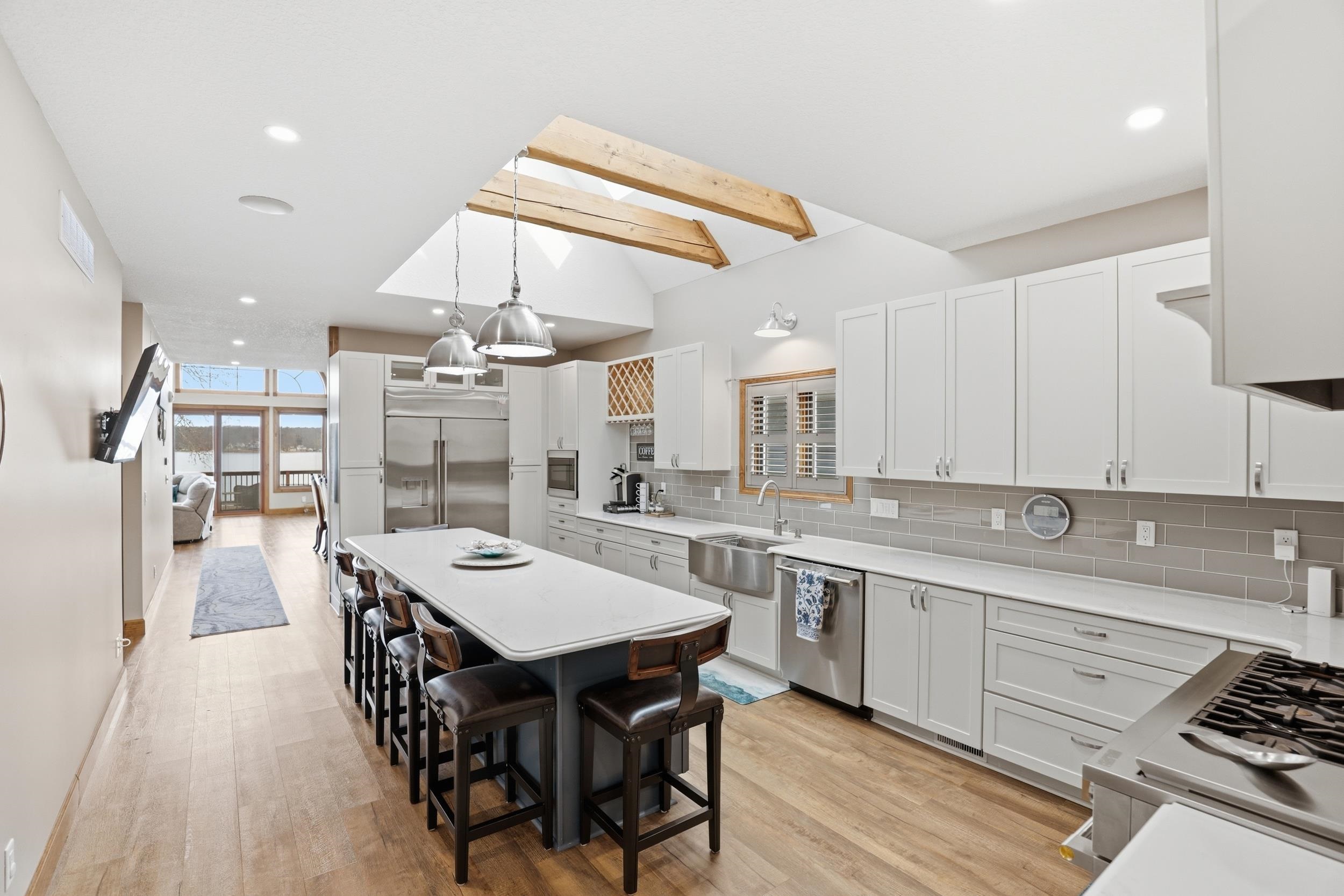 Kitchen with a skylight, white cabinets, hanging light fixtures, built in appliances, and a center island