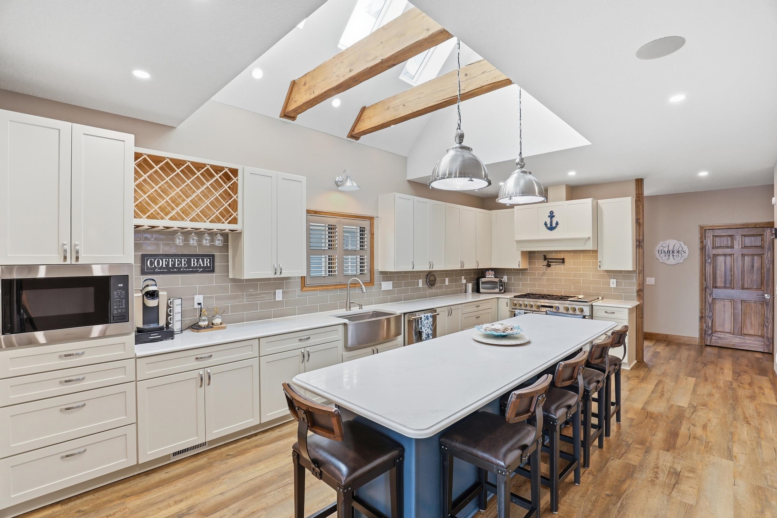 Two tone kitchen featuring a kitchen bar, decorative light fixtures, light wood-style flooring, vaulted ceiling with beams, and two tone color scheme