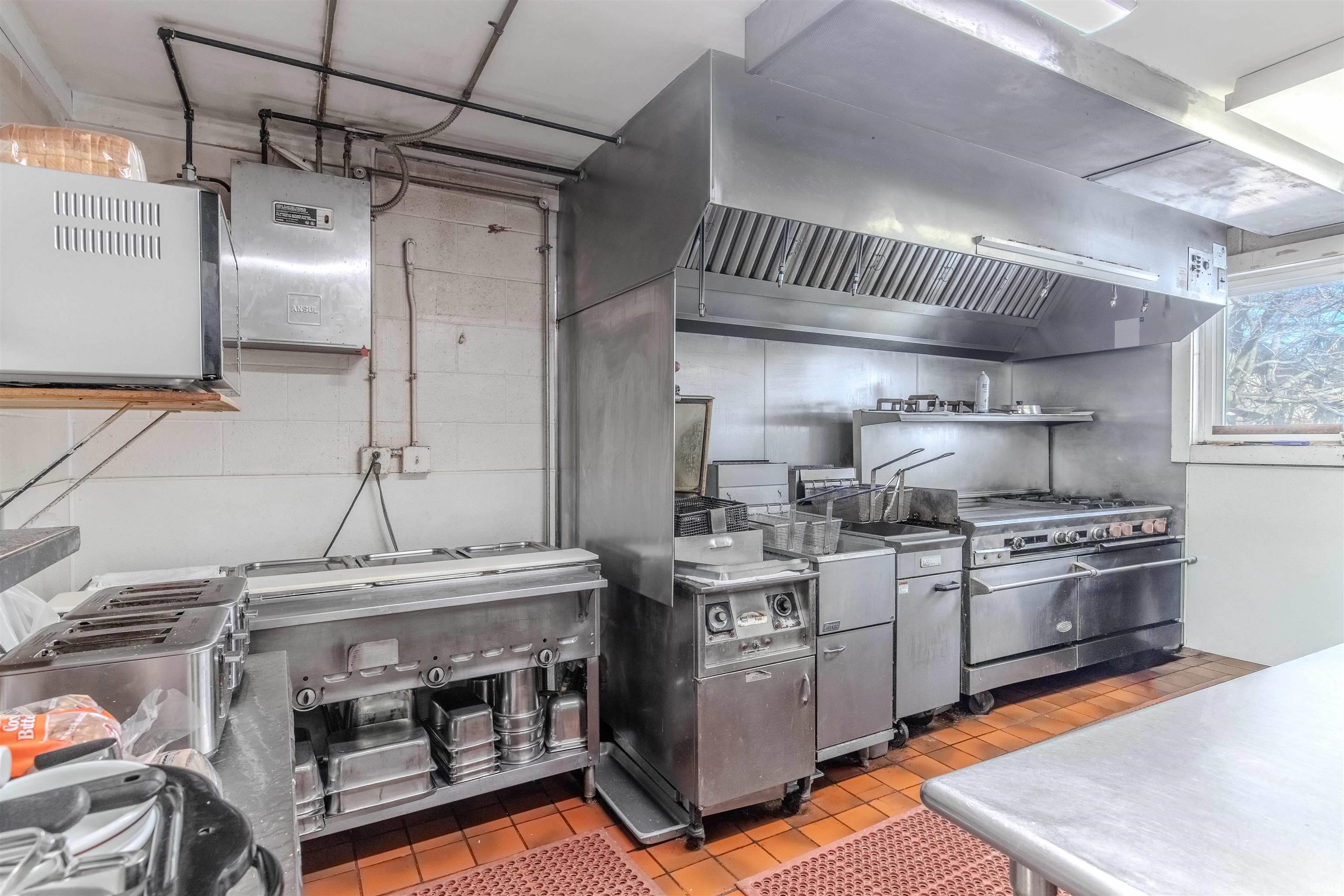 Kitchen featuring range hood, stainless steel countertops, gas stove, and open shelves
