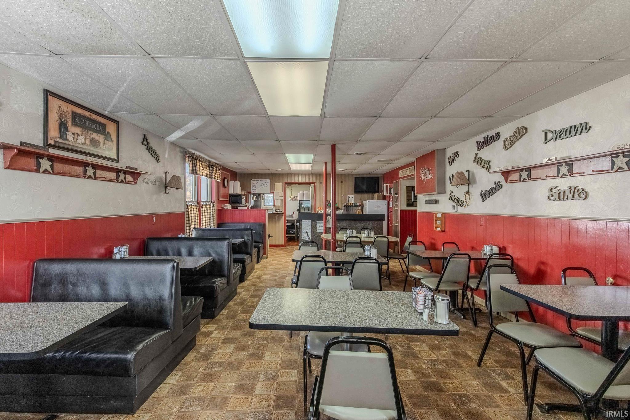Dining space featuring wainscoting, a drop ceiling, wooden walls, and tile patterned floors