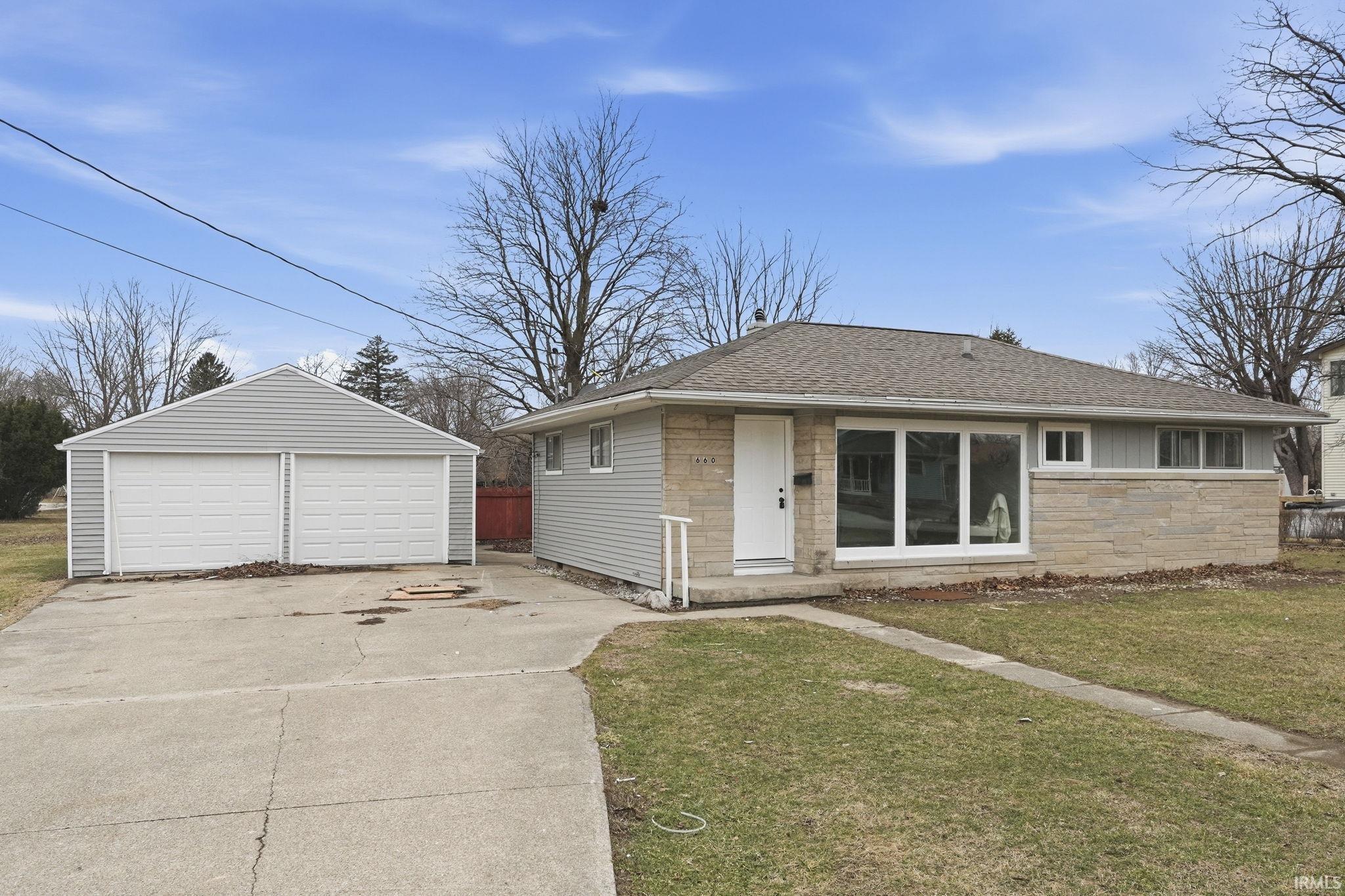 View of front of house featuring a shingled roof, an outbuilding, a garage, and a front lawn