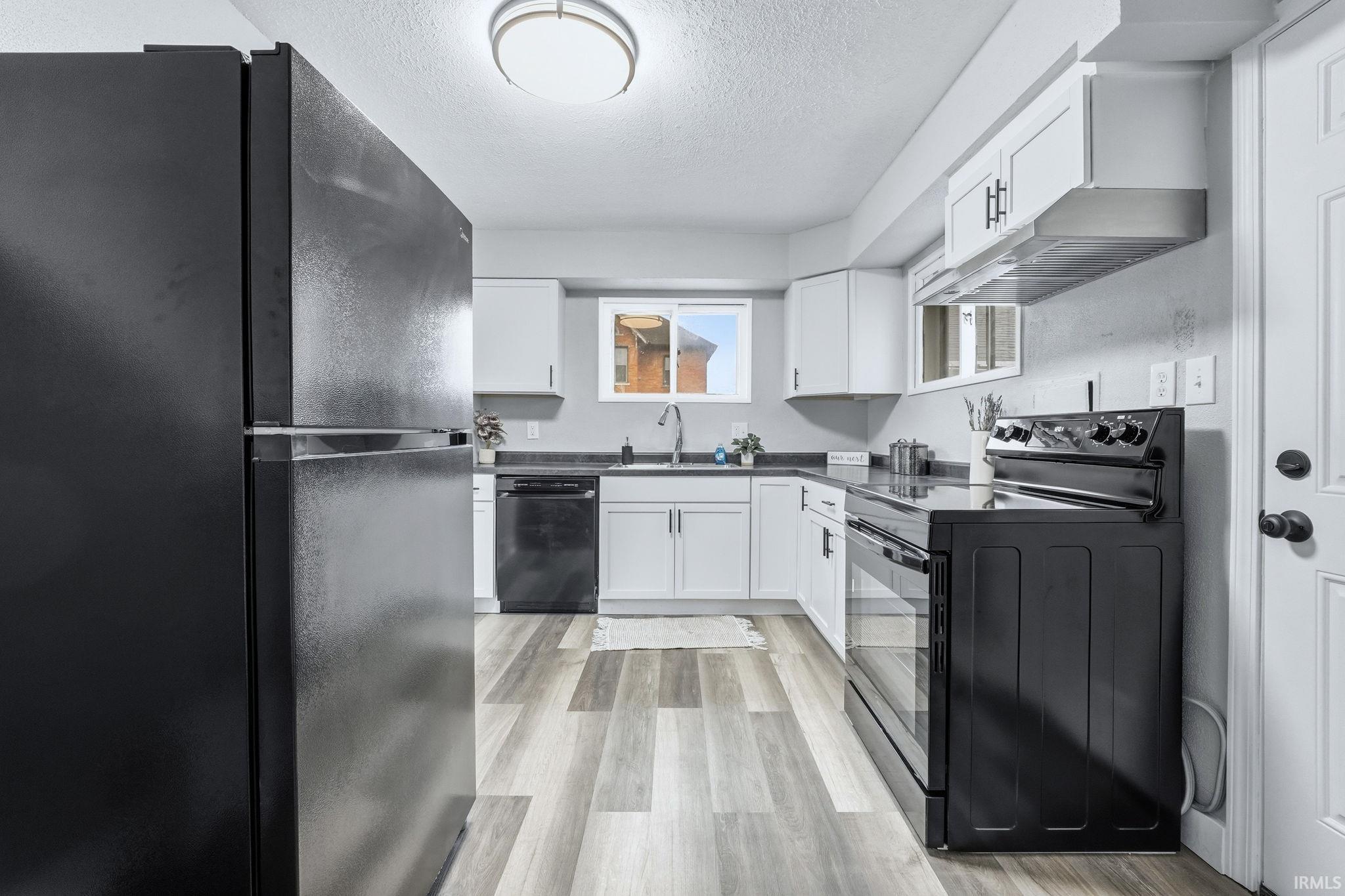 Kitchen featuring black appliances, a textured ceiling, light wood finished floors, white cabinets, and washer / clothes dryer