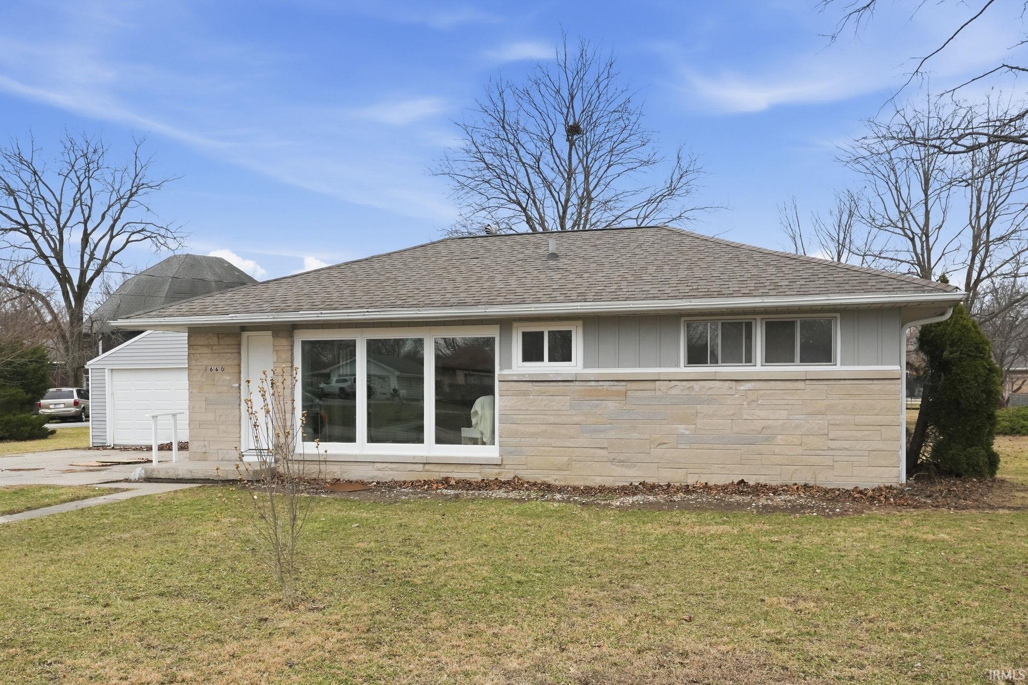 Back of house featuring roof with shingles, stone siding, and a yard