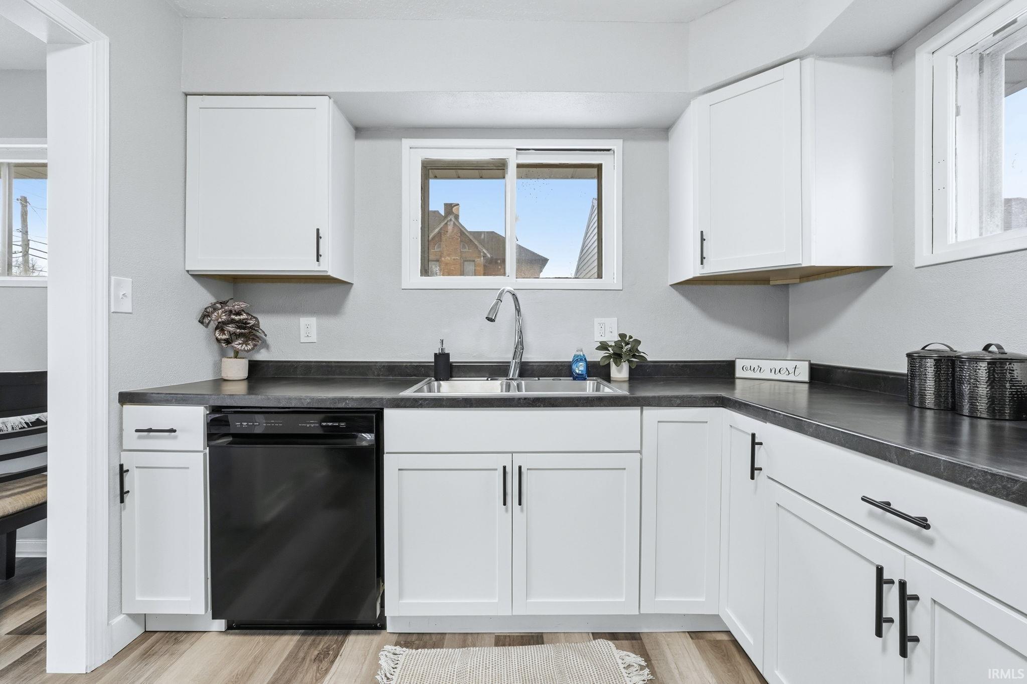 Kitchen featuring dark countertops, dishwasher, white cabinets, and light wood-style flooring