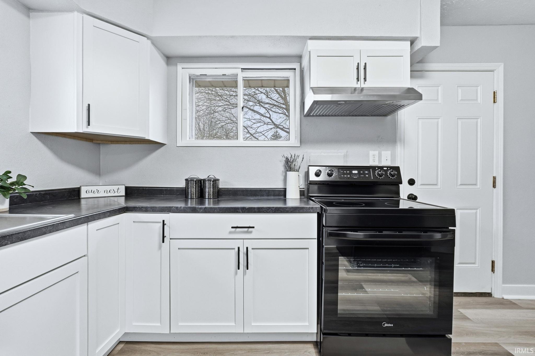Kitchen with black range with electric stovetop, dark countertops, white cabinets, and light wood-type flooring