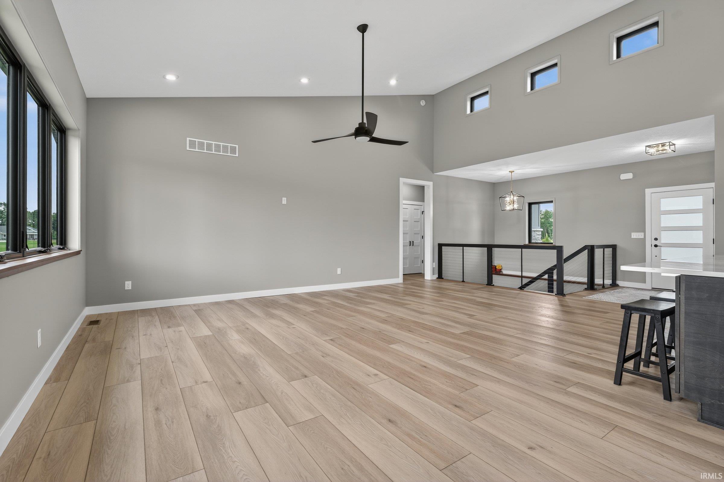 Living room with a ceiling fan, light wood-style floors, hanging lights, and a high ceiling