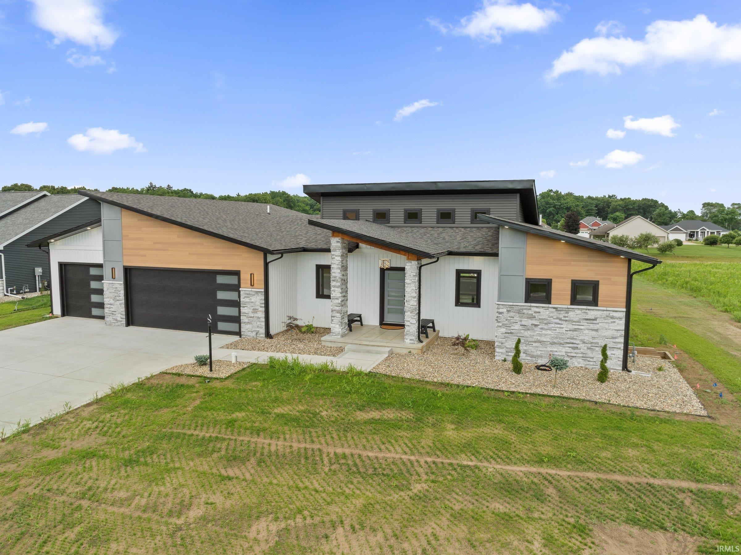 Contemporary home featuring stone siding, a garage, a front lawn, driveway, and roof with shingles