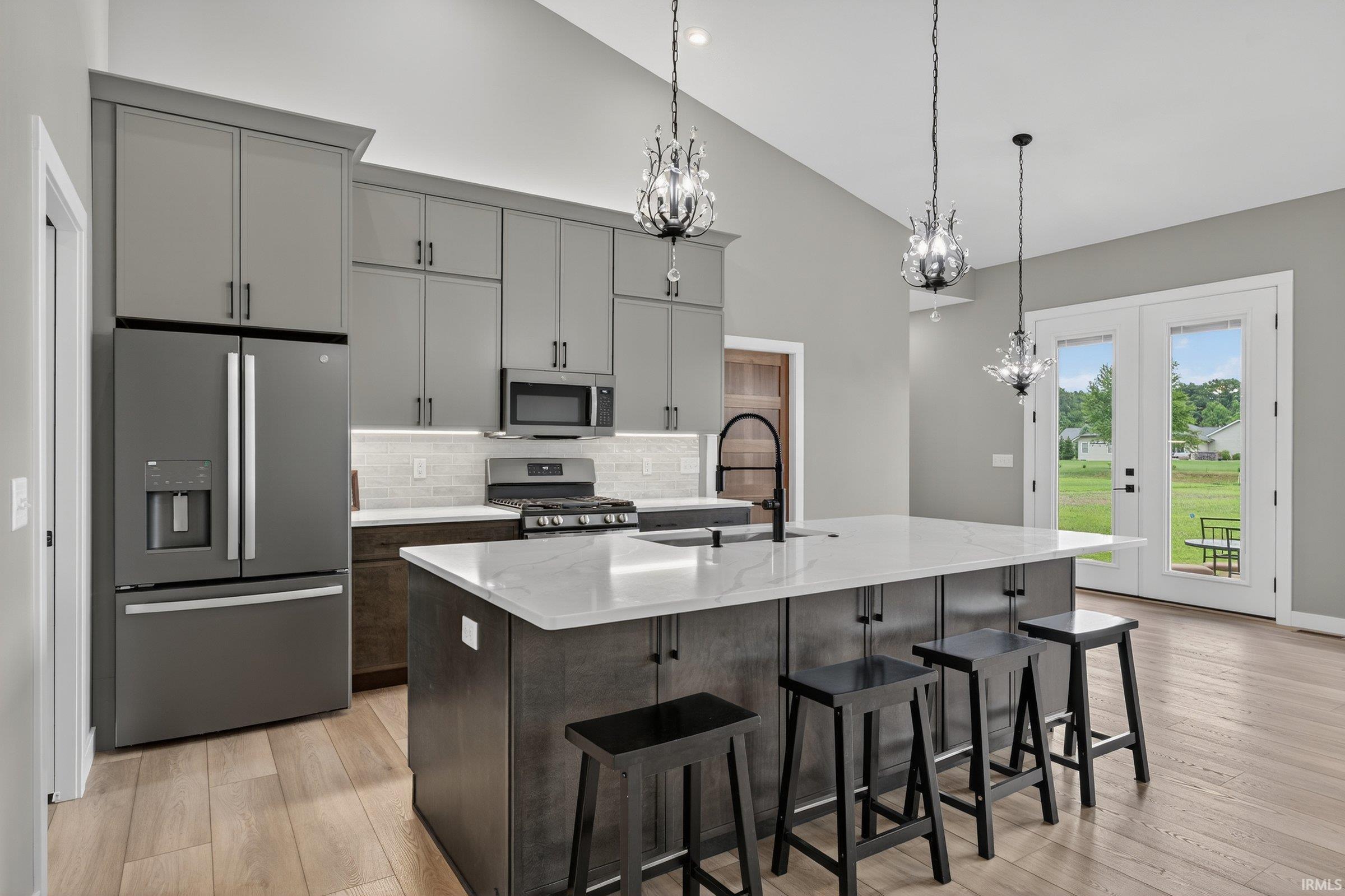 Dual tone kitchen with stainless steel appliances, a chandelier, light stone countertops, a breakfast bar area, and lofted ceiling