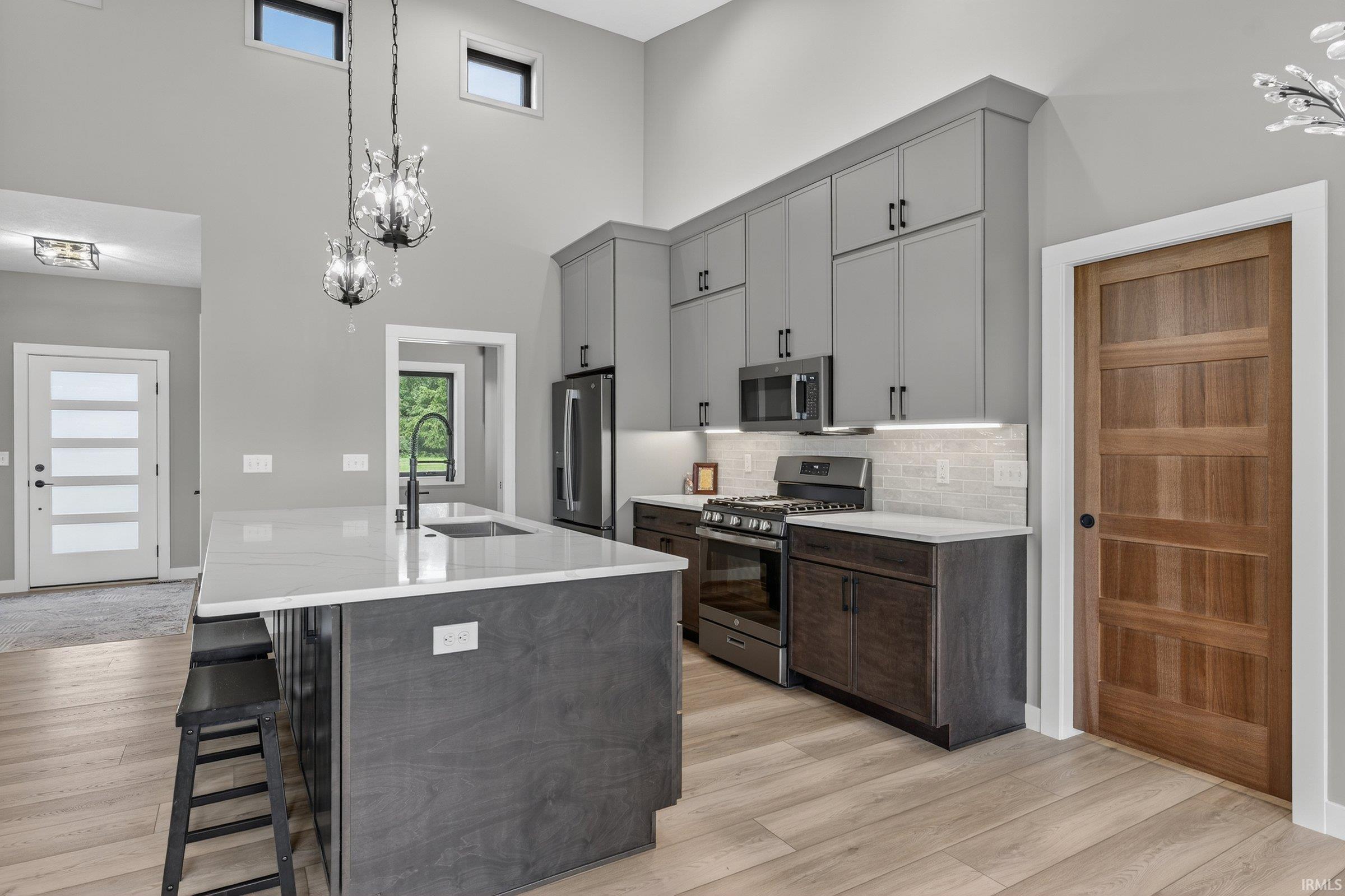 Kitchen with a chandelier, a breakfast bar area, stainless steel appliances, light stone countertops, and light wood-type flooring