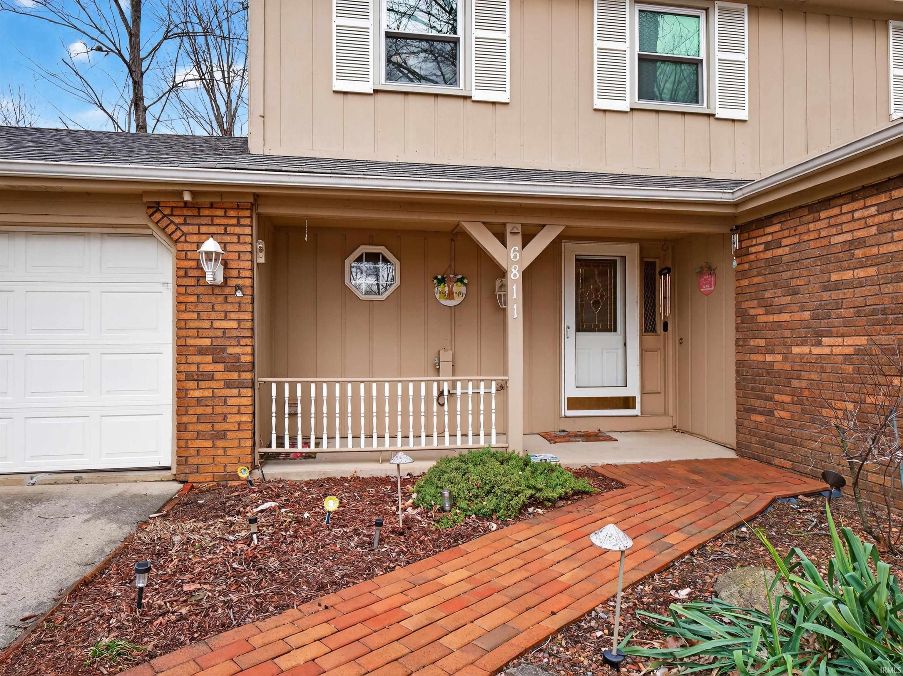 Doorway to property featuring a porch, brick siding, and roof with shingles