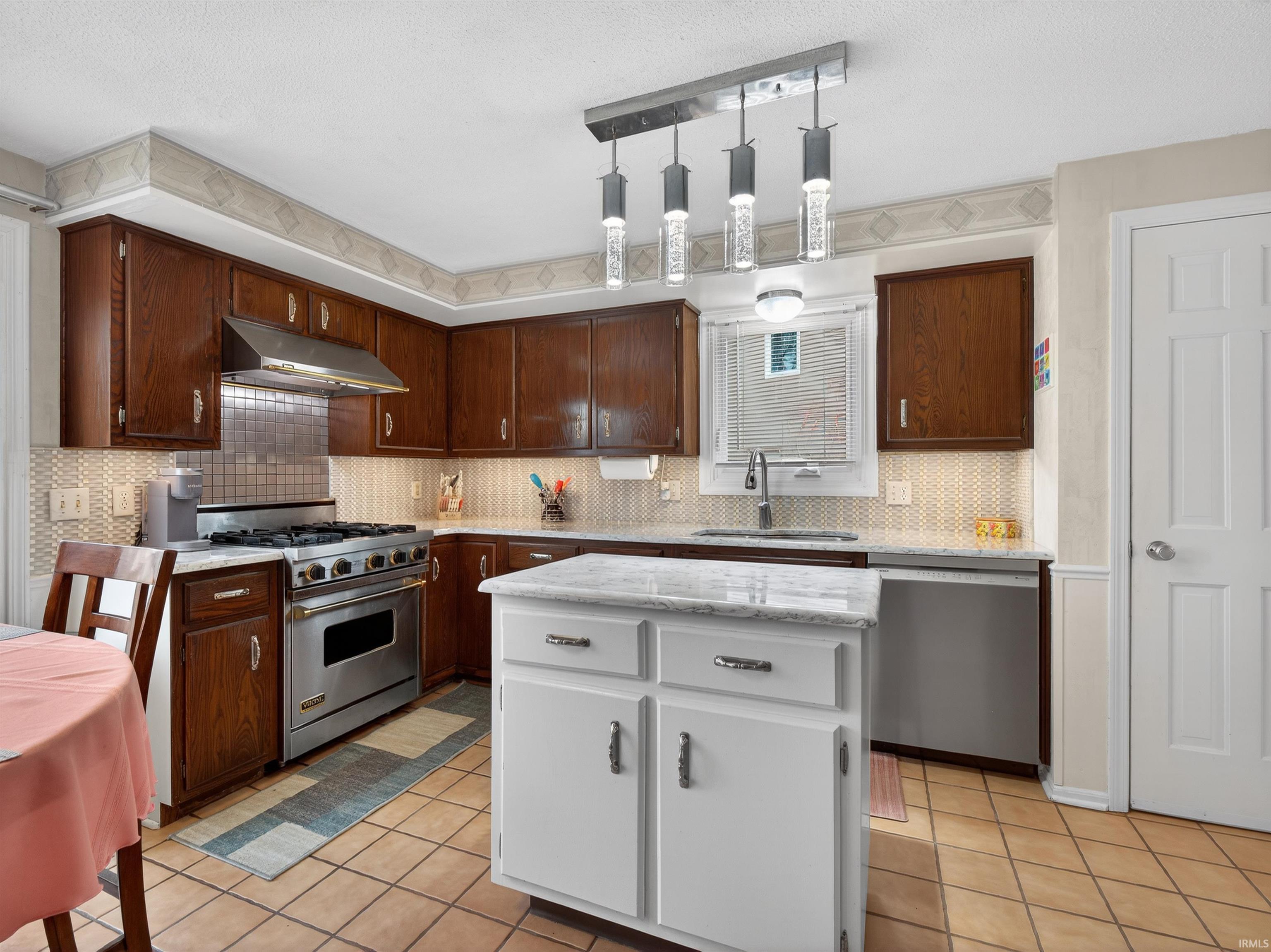 Kitchen with stainless steel appliances, light tile patterned floors, a center island, pendant lighting, and tasteful backsplash