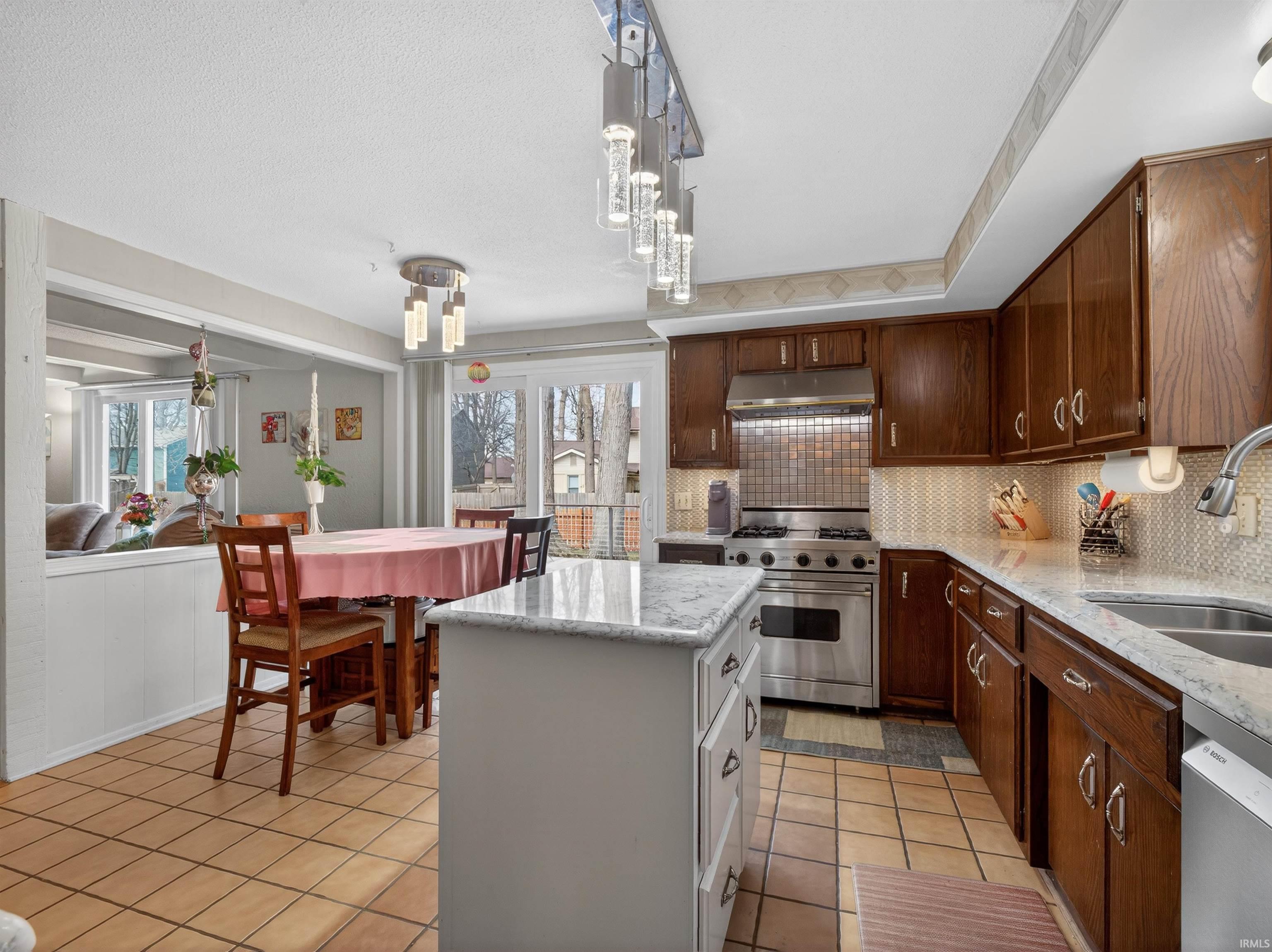 Dual tone kitchen featuring stainless steel appliances, light tile patterned floors, light stone countertops, backsplash, and a center island