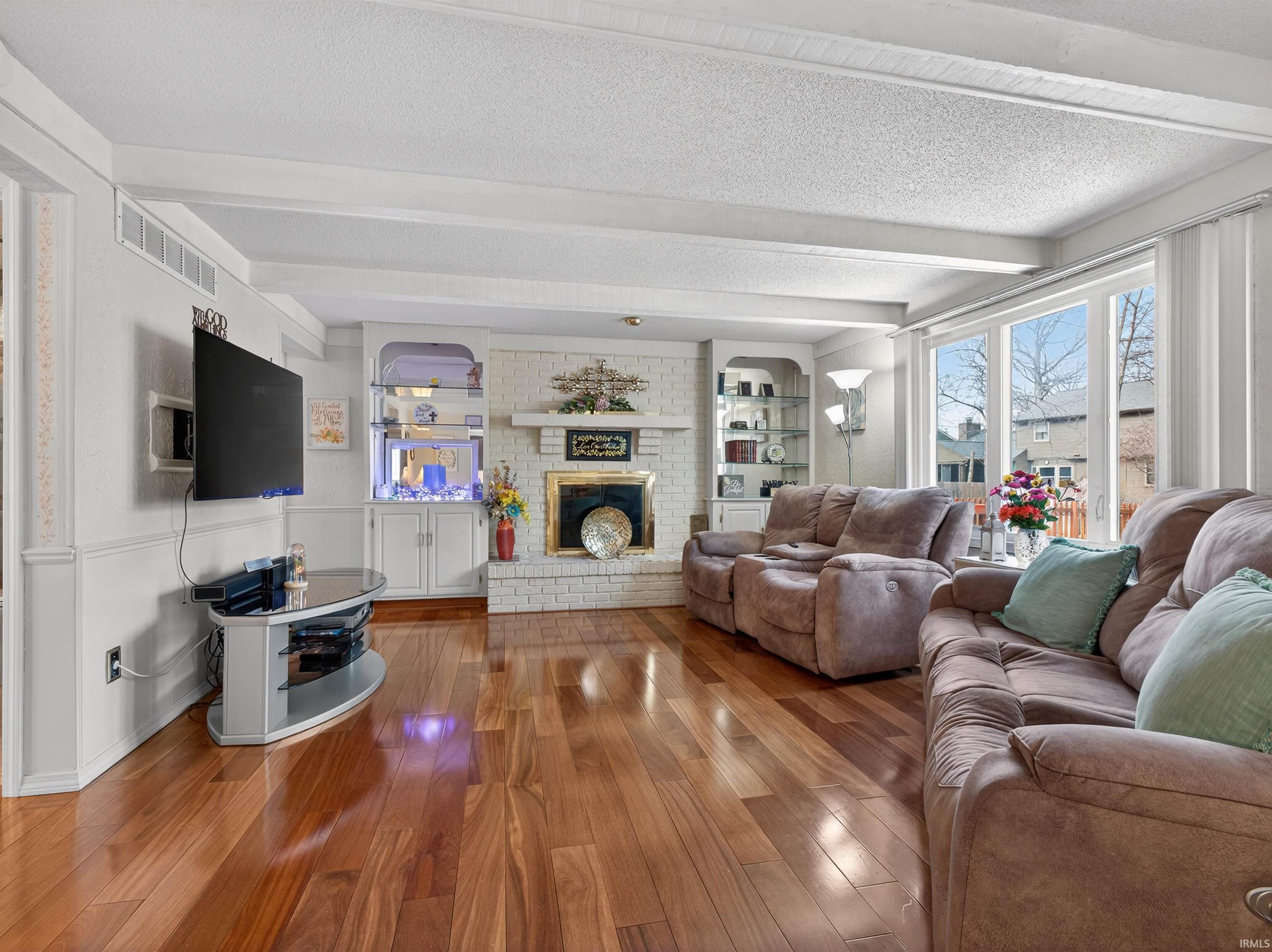 Living area with a textured ceiling, hardwood / wood-style flooring, built in features, a fireplace, and beamed ceiling