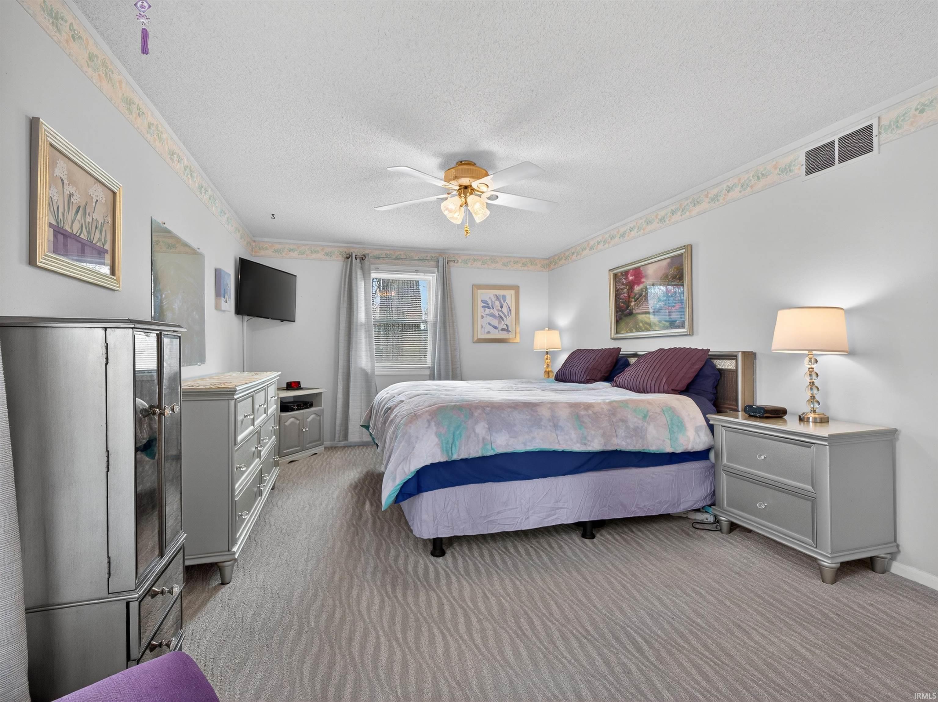 Bedroom with light colored carpet, ceiling fan, and a textured ceiling