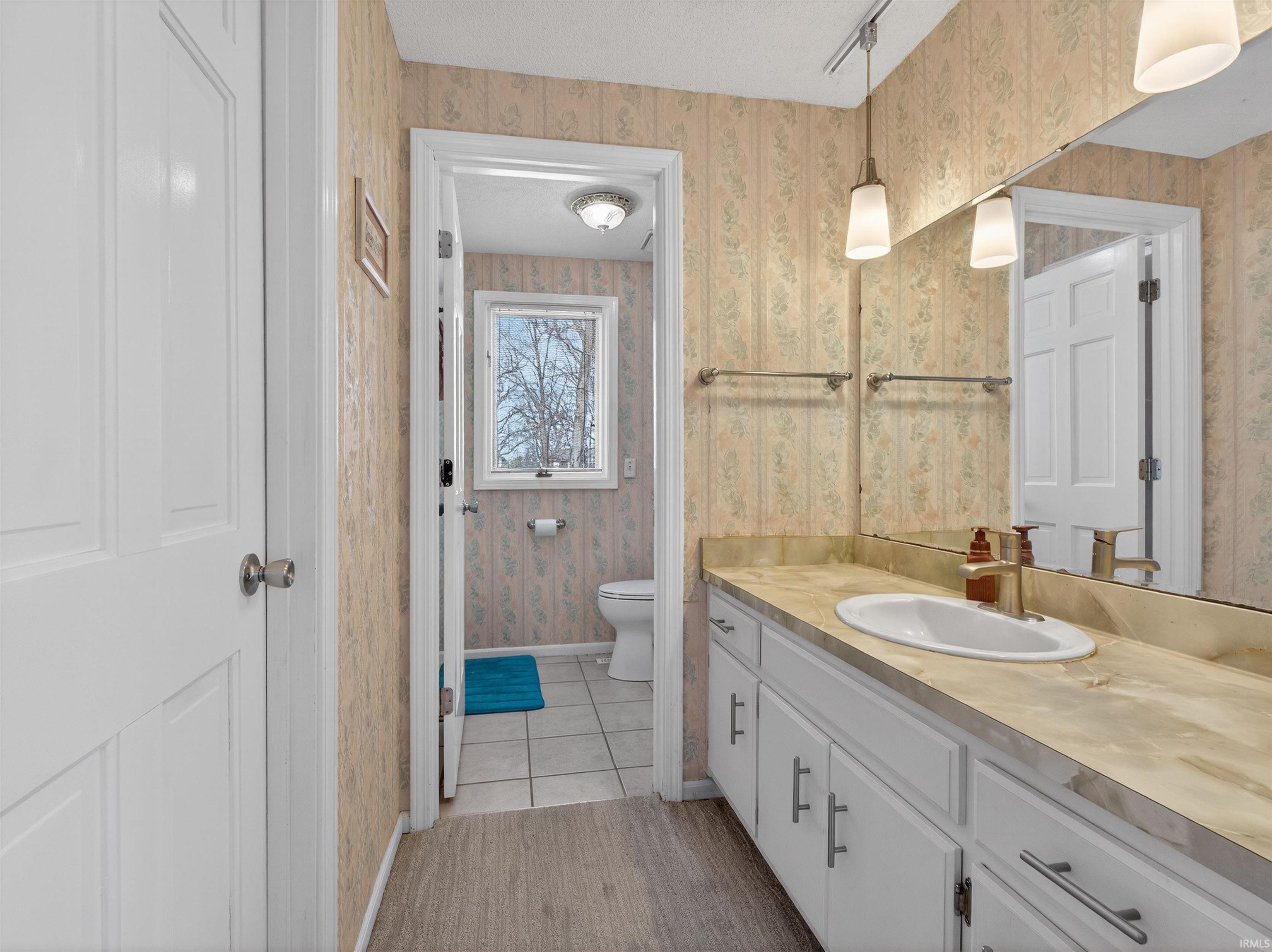Bathroom featuring vanity, light tile patterned flooring, wallpapered walls, and rail lighting
