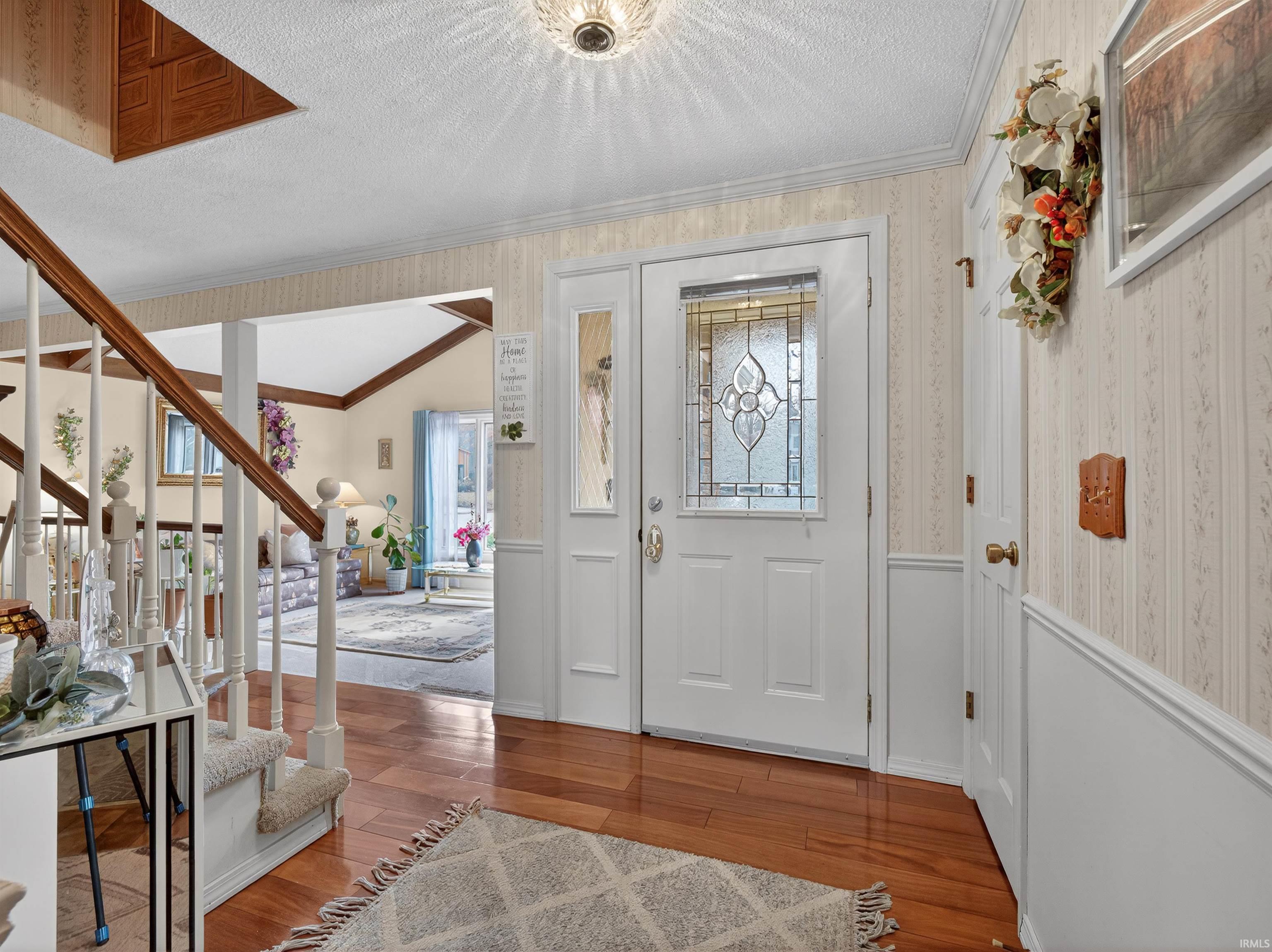 Foyer entrance with wood finished floors, wallpapered walls, wainscoting, a textured ceiling, and healthy amount of natural light