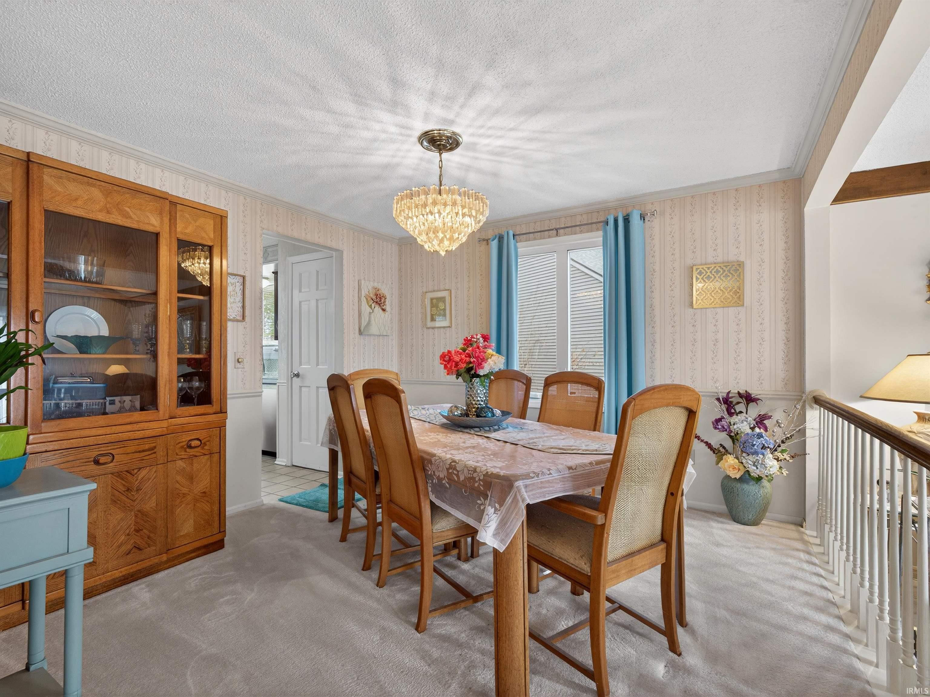 Dining room with light colored carpet, a chandelier, a textured ceiling, plenty of natural light, and wallpapered walls