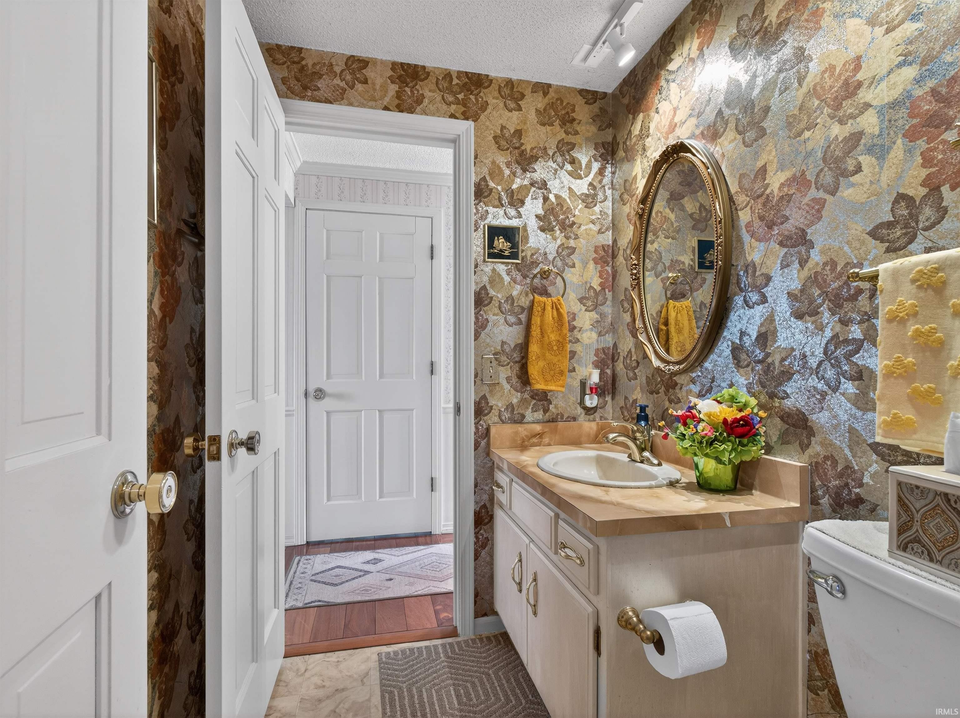 Bathroom with a textured ceiling, vanity, track lighting, and wallpapered walls