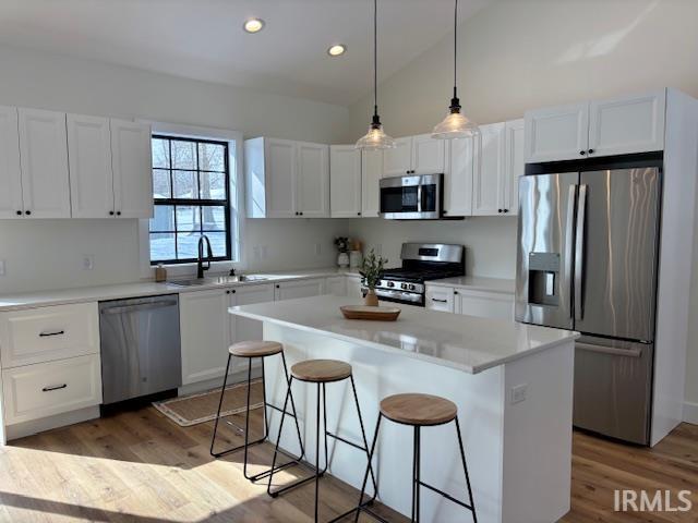 Kitchen with stainless steel appliances, a breakfast bar area, white cabinetry, and vaulted ceiling