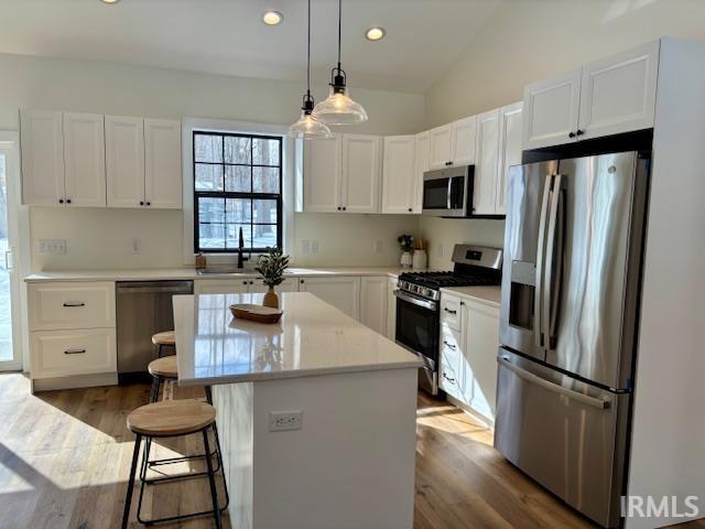 Kitchen featuring stainless steel appliances, a center island, white cabinets, hanging light fixtures, and dark wood-style flooring