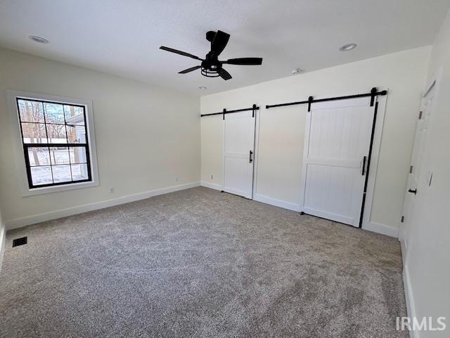 Unfurnished bedroom featuring a barn door, light carpet, and ceiling fan