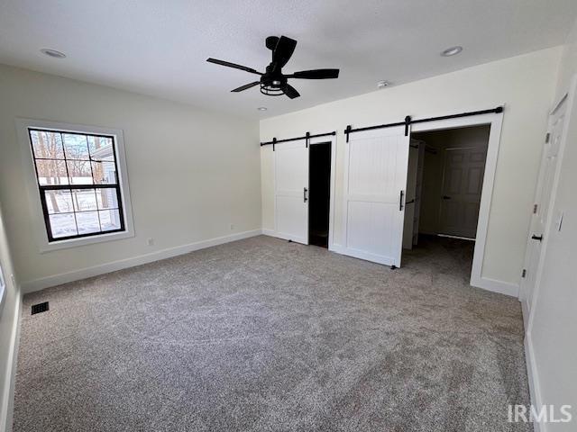 Unfurnished bedroom featuring a barn door, light carpet, and a ceiling fan with barn doors opening to private bath and walk-n closet.