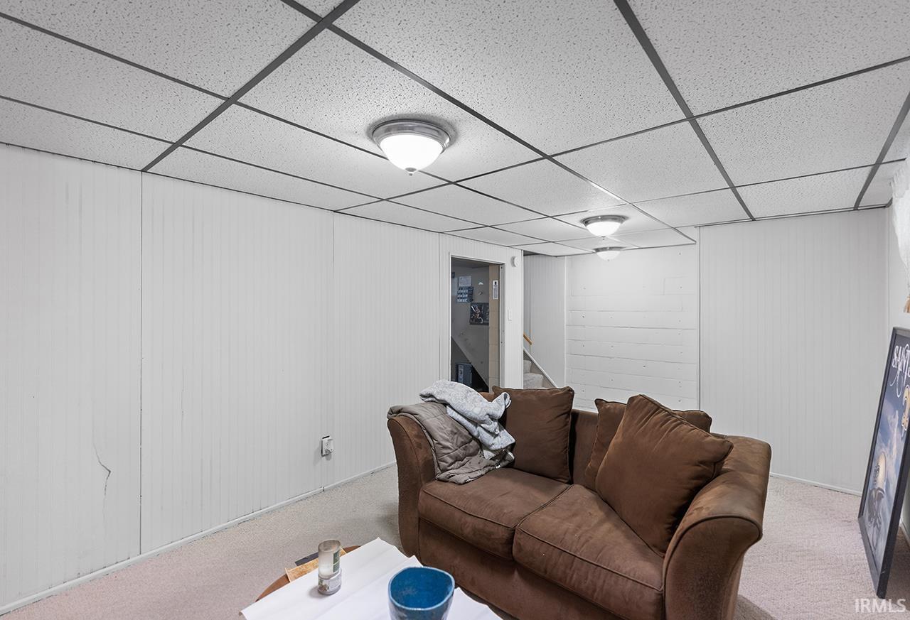Carpeted living room featuring wood walls and a drop ceiling