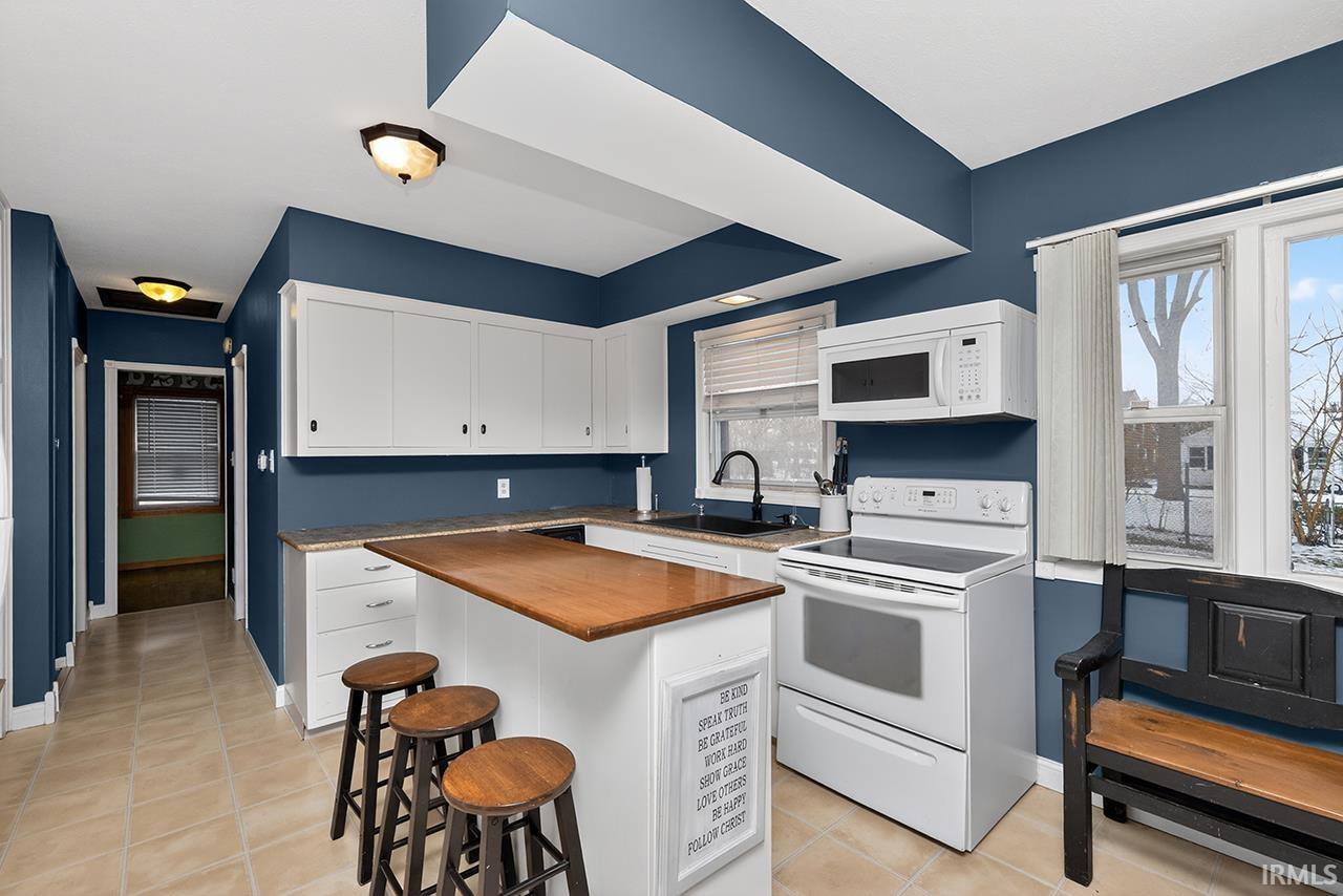 Kitchen with white appliances, wooden counters, a breakfast bar, light tile patterned flooring, and white cabinets