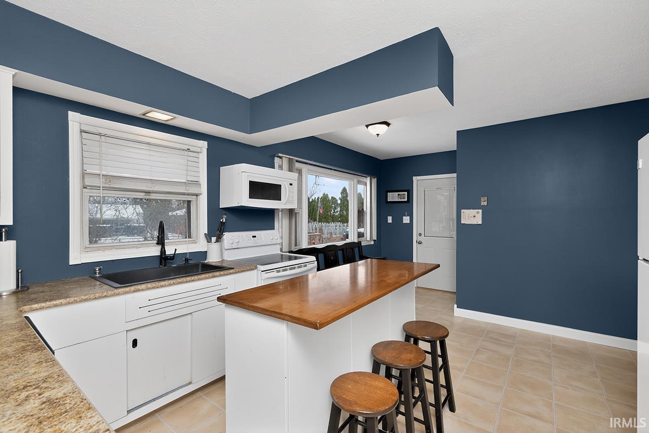 Kitchen featuring butcher block counters, white cabinets, a breakfast bar, white appliances, and a kitchen island