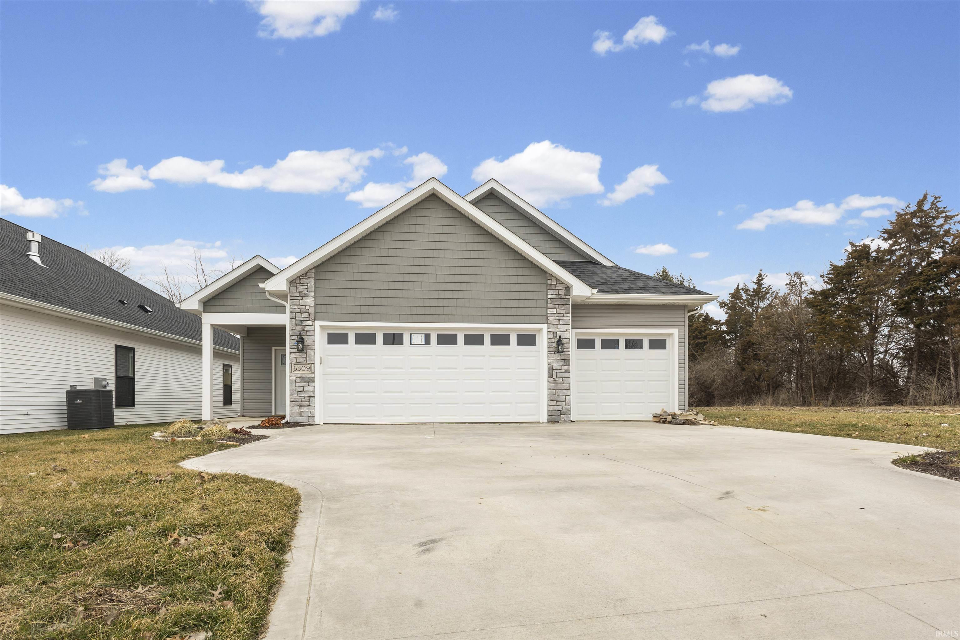 View of front facade featuring stone siding, a garage, driveway, and a front lawn