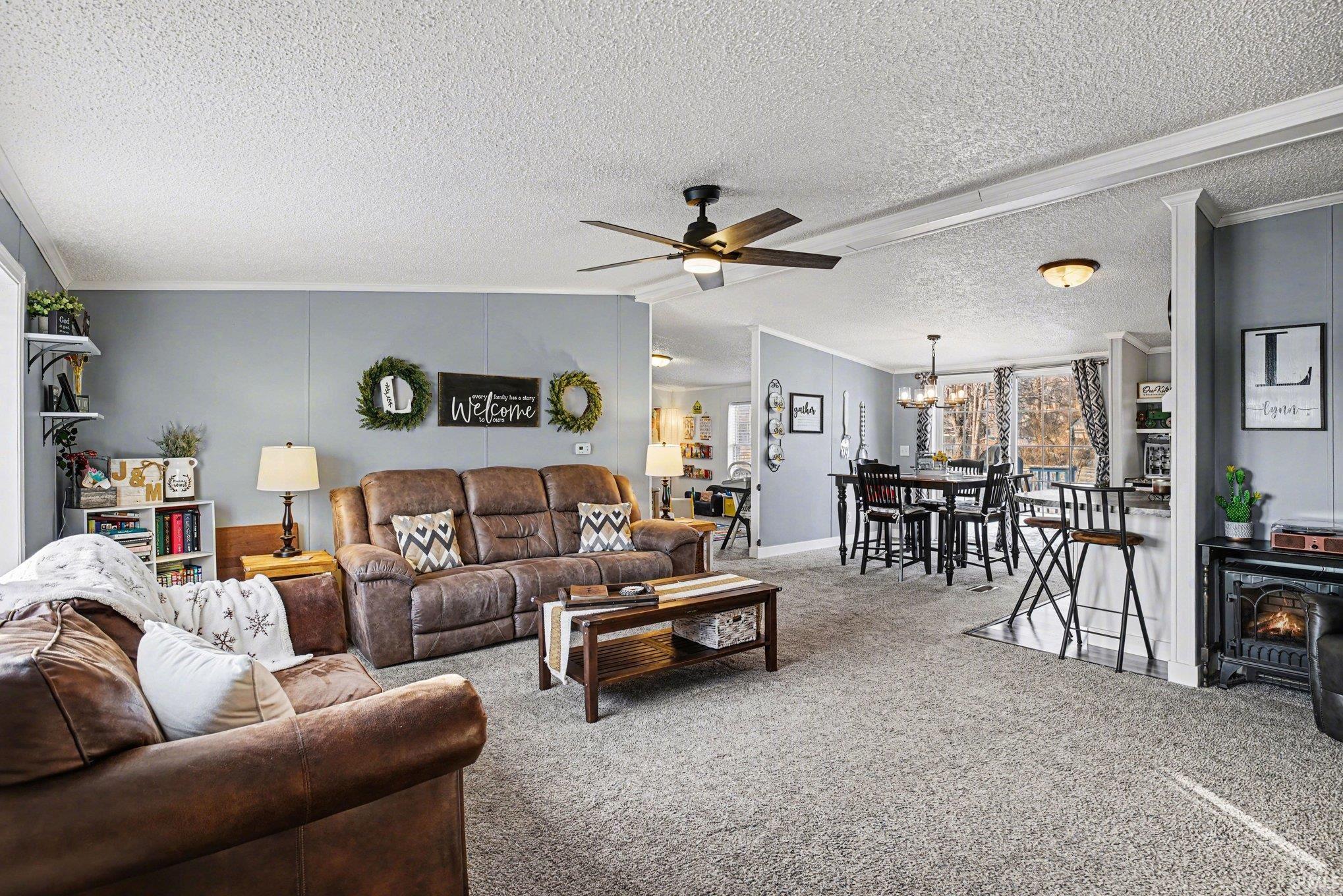 Carpeted living room with crown molding, a ceiling fan, a wood stove, a textured ceiling, and a chandelier