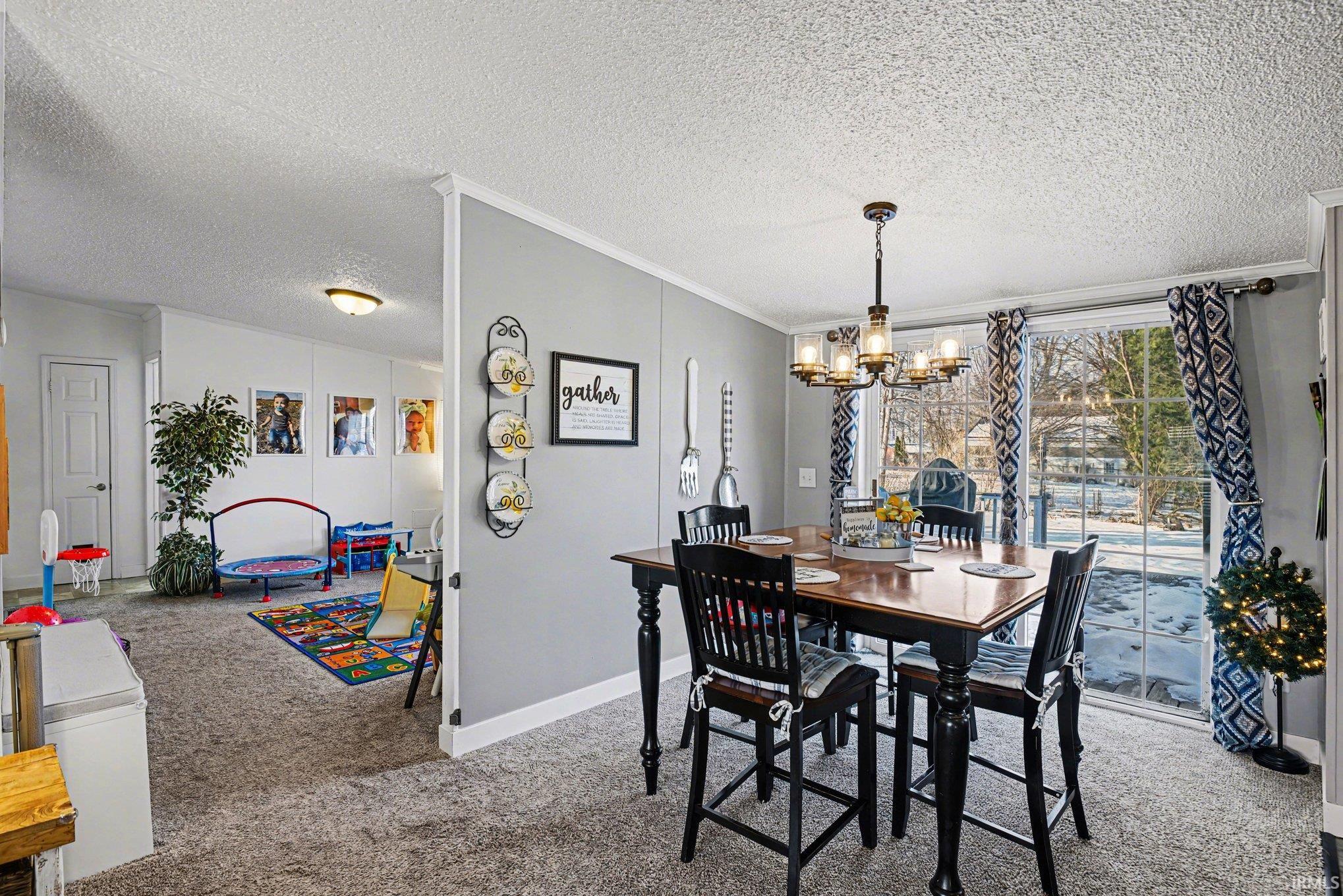 Dining room with light colored carpet, a textured ceiling, ornamental molding, and a chandelier