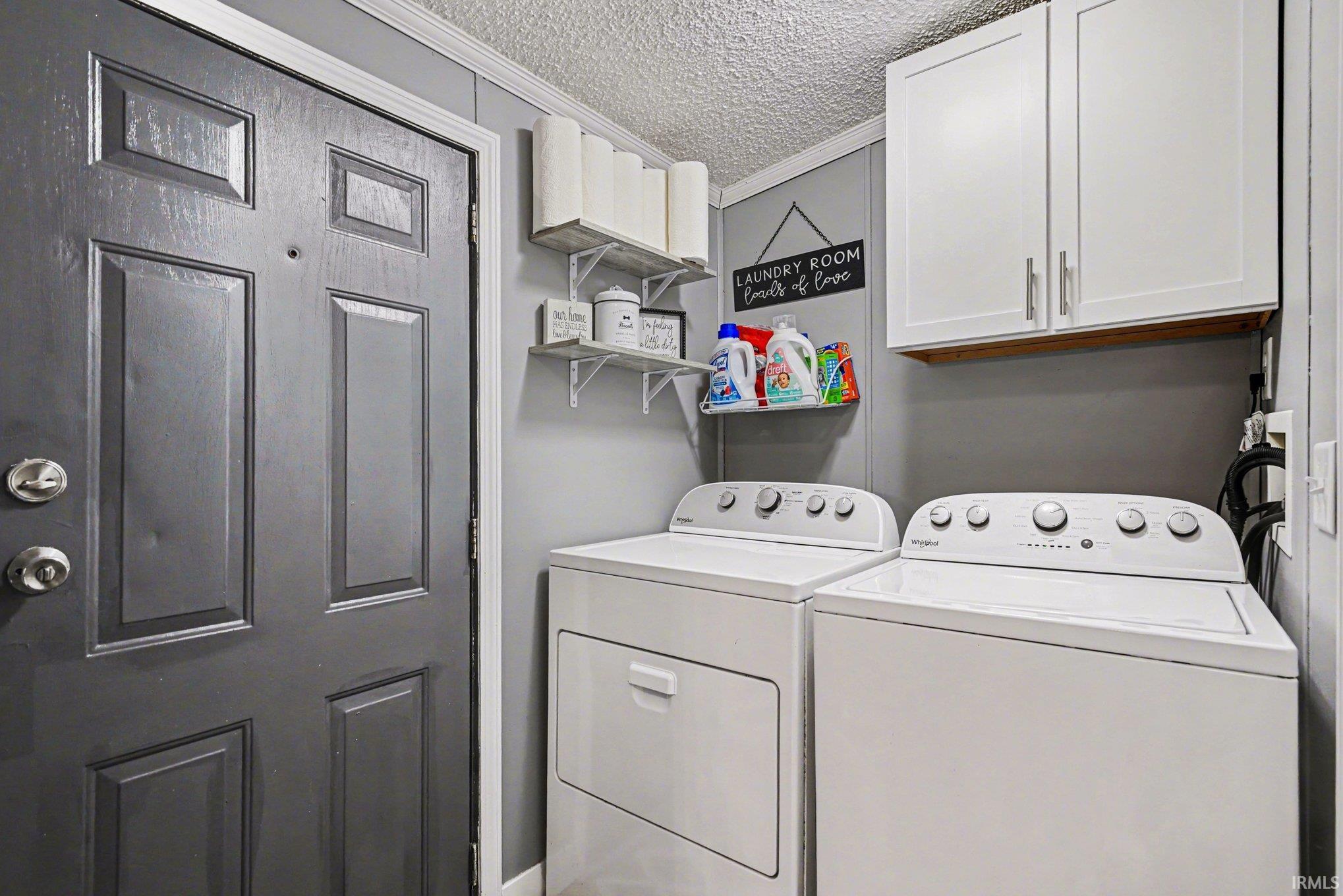 Laundry room with a textured ceiling, washing machine and clothes dryer, crown molding, and cabinet space
