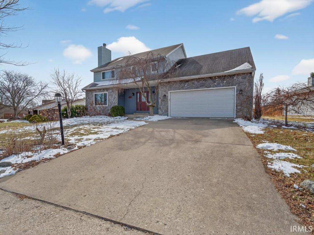 Traditional home with stone siding, an attached garage, concrete driveway, and a chimney